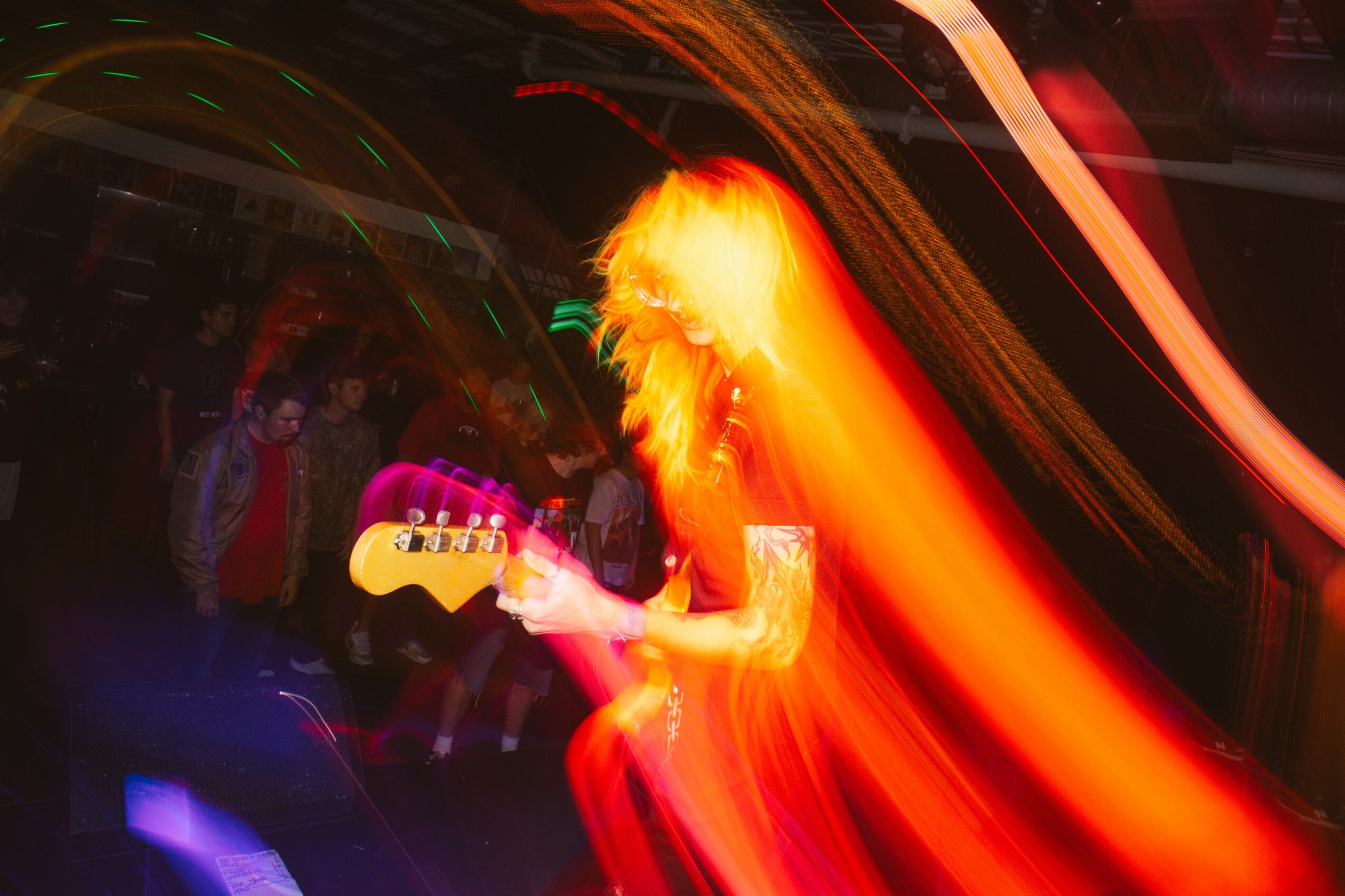 Person playing guitar on stage with bright, colorful light trails and a crowd in the background.