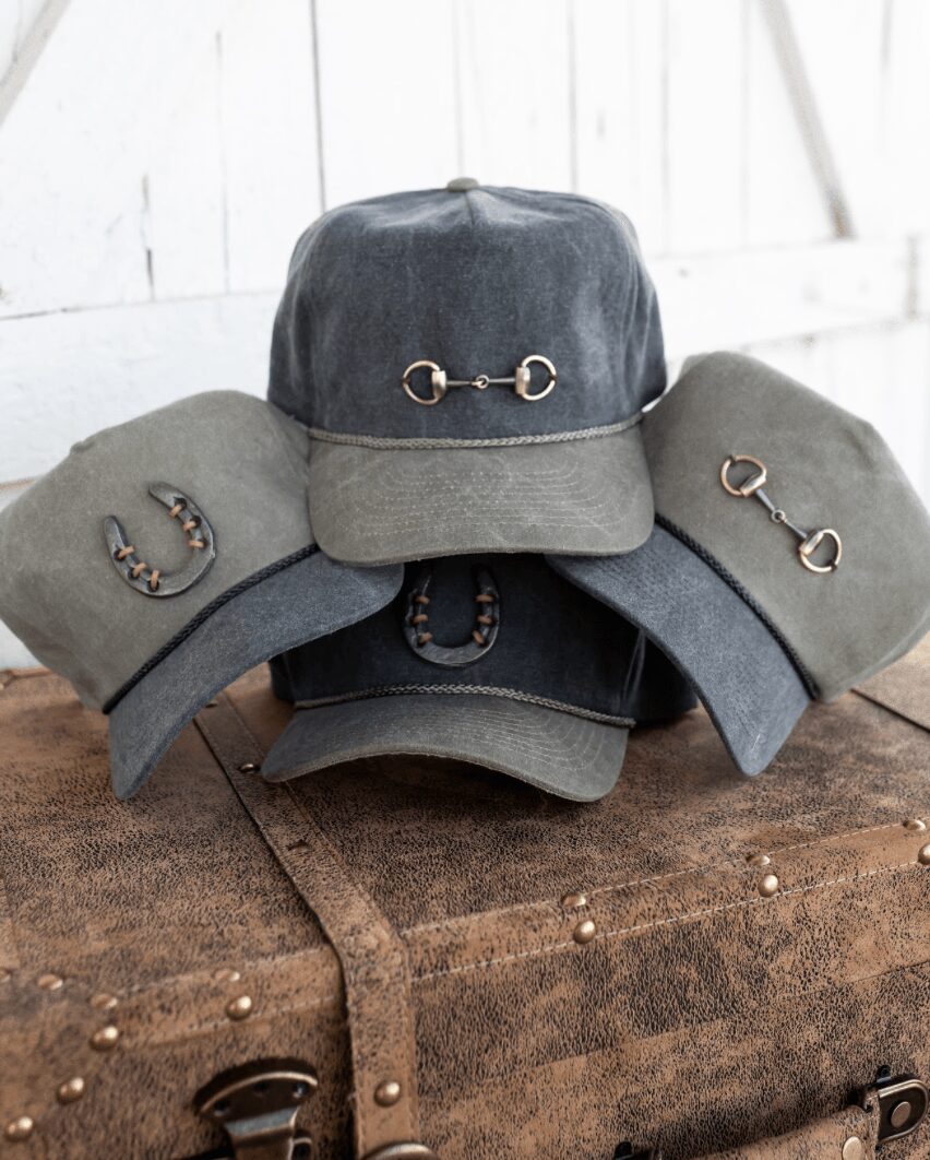 Five caps with horsebit details arranged on a wooden surface against a white wall background.