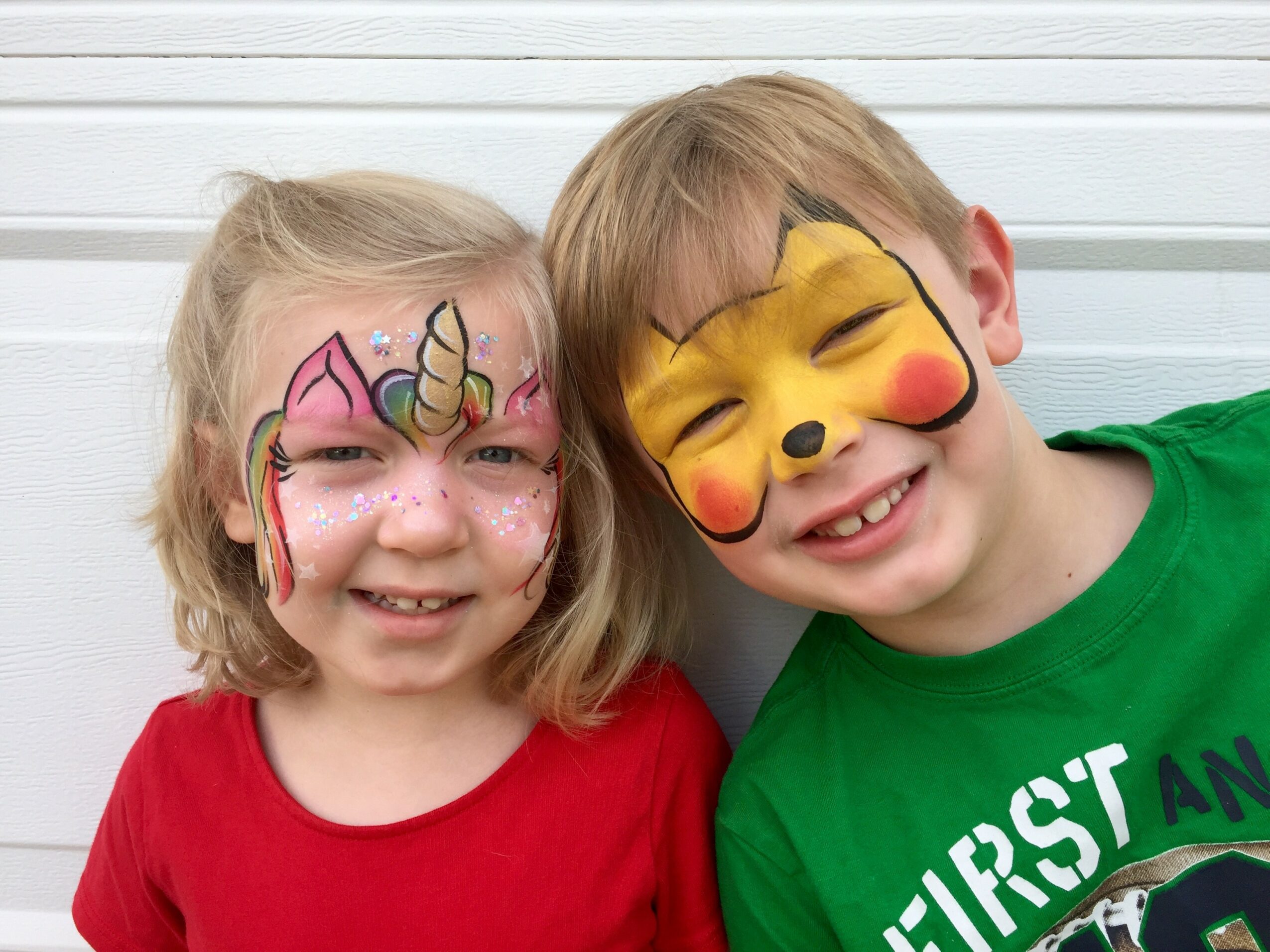 Two children with face paint, smiling, close together, against a white background.