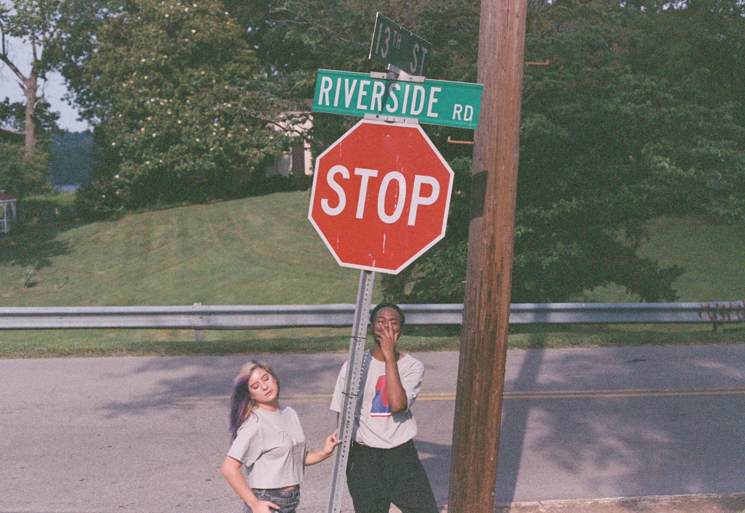 Two children standing near a stop sign at Riverside Road, with trees and a road in the background.