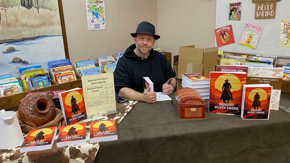 Man sitting at a table with books and promotional materials, in a room with posters and a window showing snow outside.