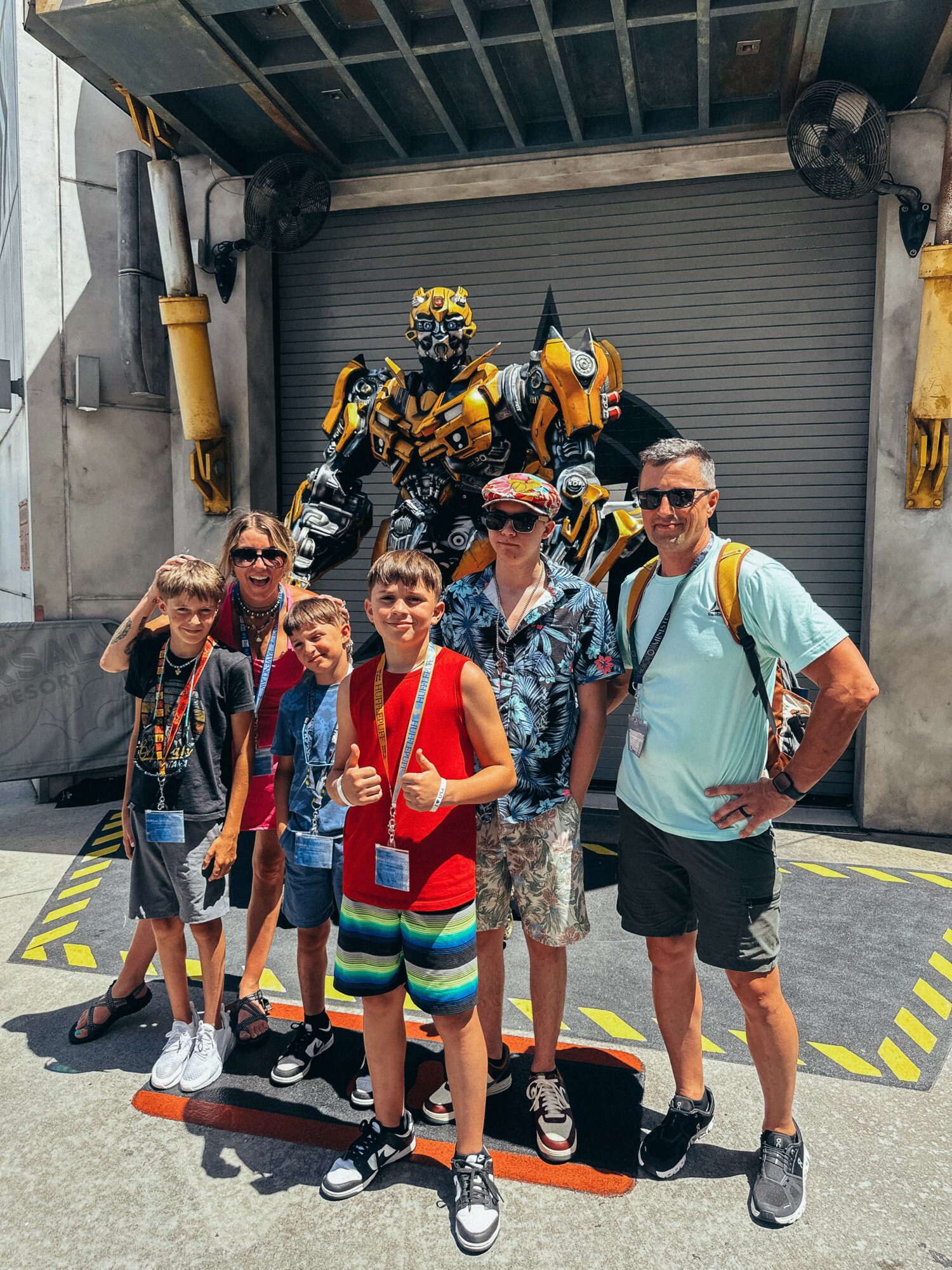 Group of six people, including children and adults, posing in front of a large robot figure at an amusement park.