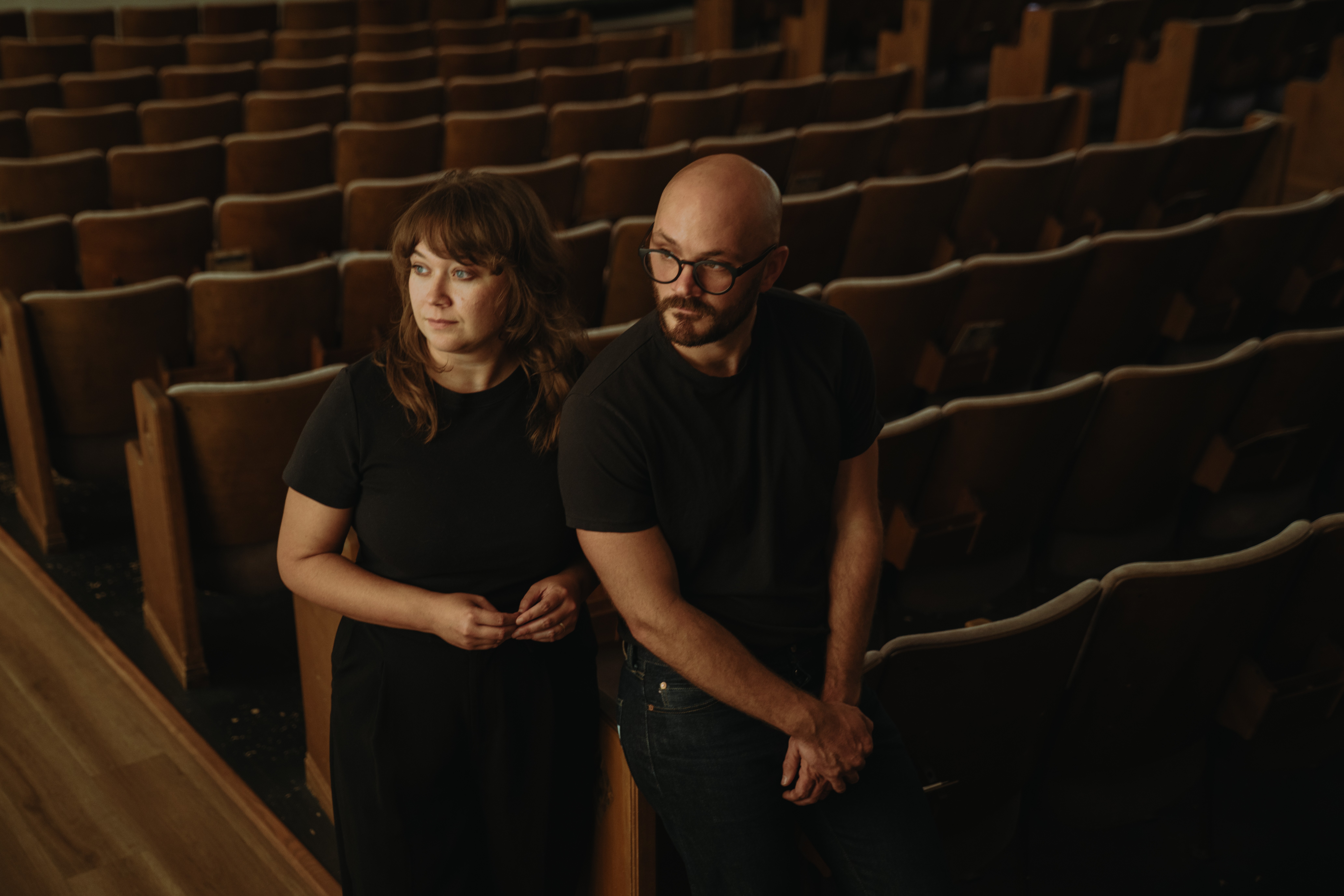 Two people standing in an empty auditorium with rows of seats behind them.