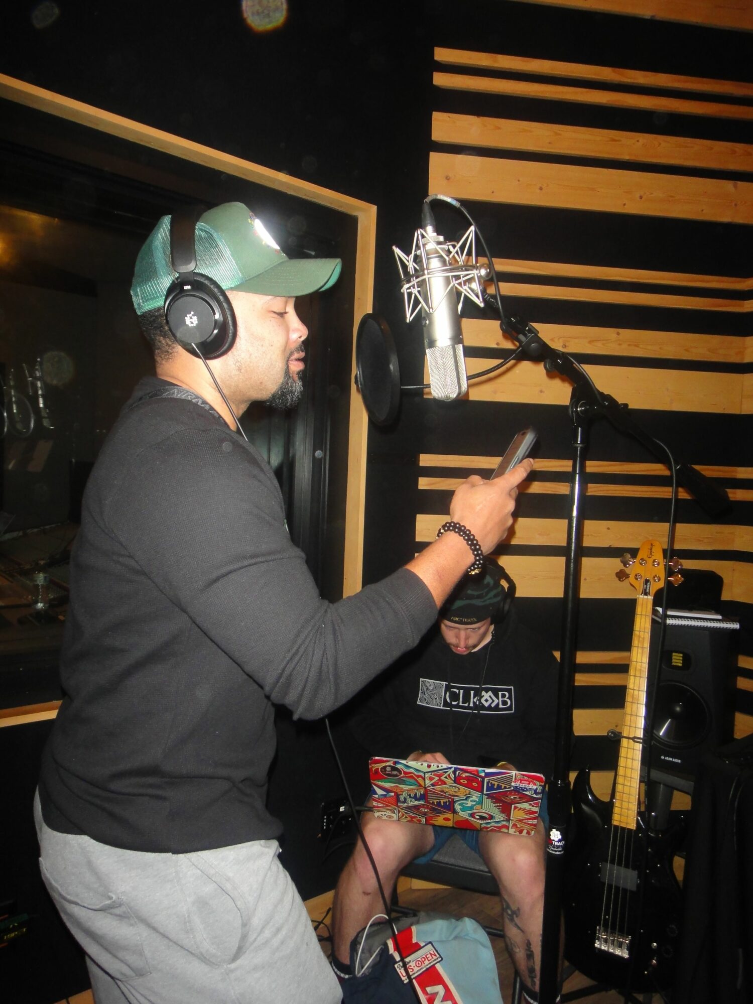 Person wearing headphones and a cap, recording vocals in a studio with a microphone and soundproof walls.