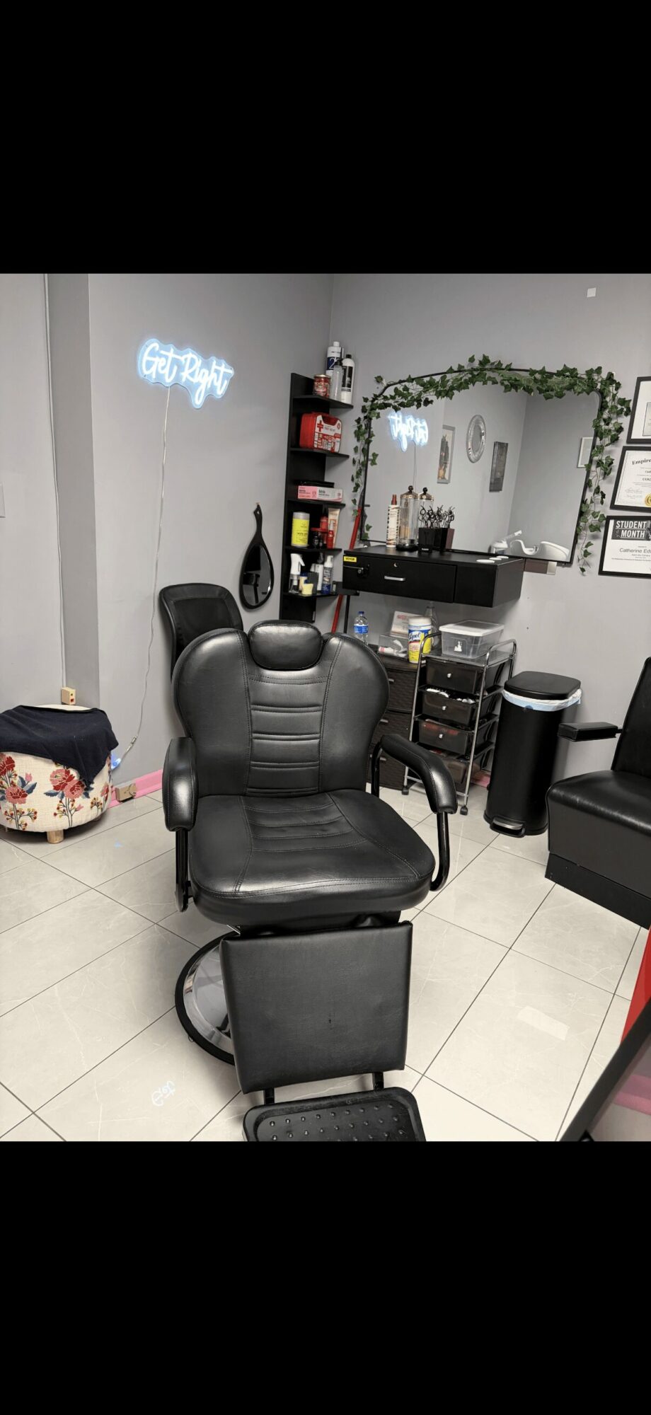 Salon chair in front of mirror with shelves and decor, white tiled floor, and wall-mounted mirror.