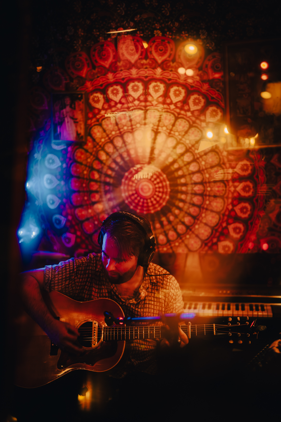 Person playing guitar in a dimly lit room with colorful, circular light patterns on the wall behind.