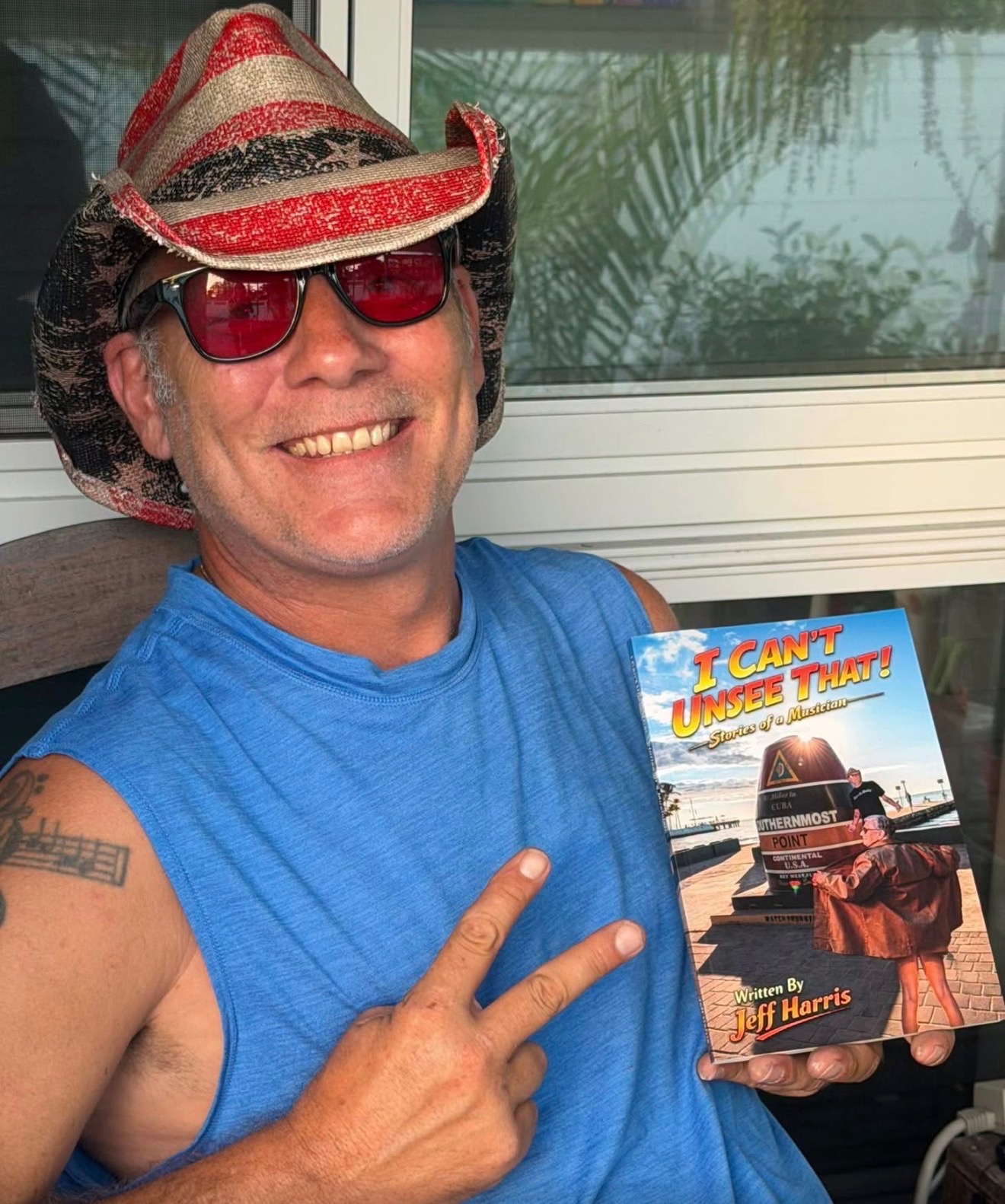 Person wearing a cowboy hat and sunglasses, smiling, holding a book titled 