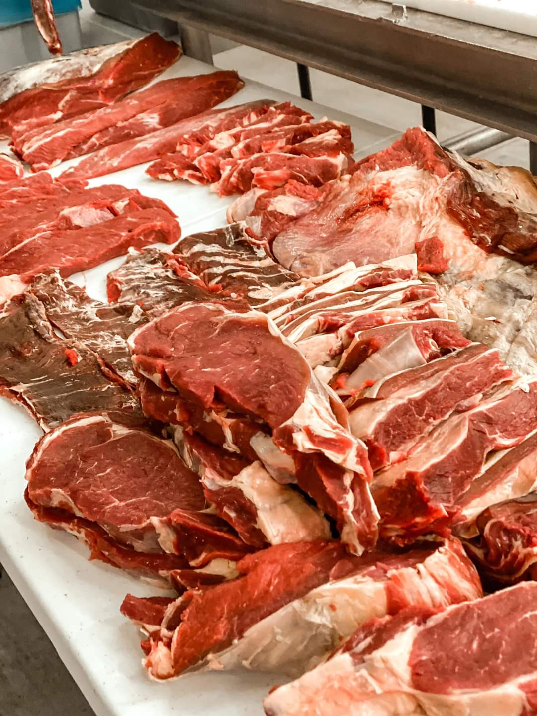 Various cuts of raw red meat displayed on a white surface, with some marbled and others lean.