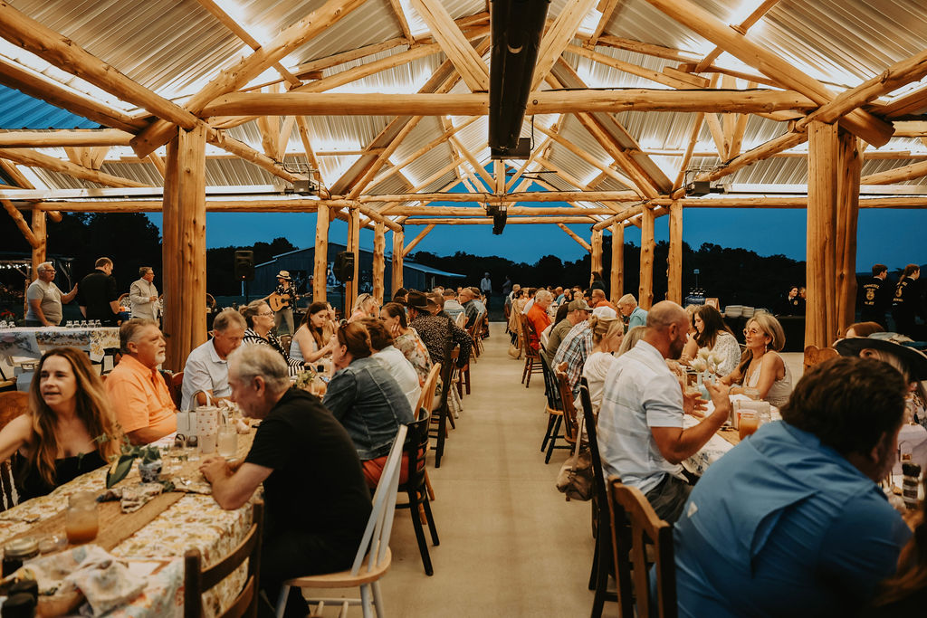 People dining at tables inside a wooden pavilion with a view of mountains and sky in the background.