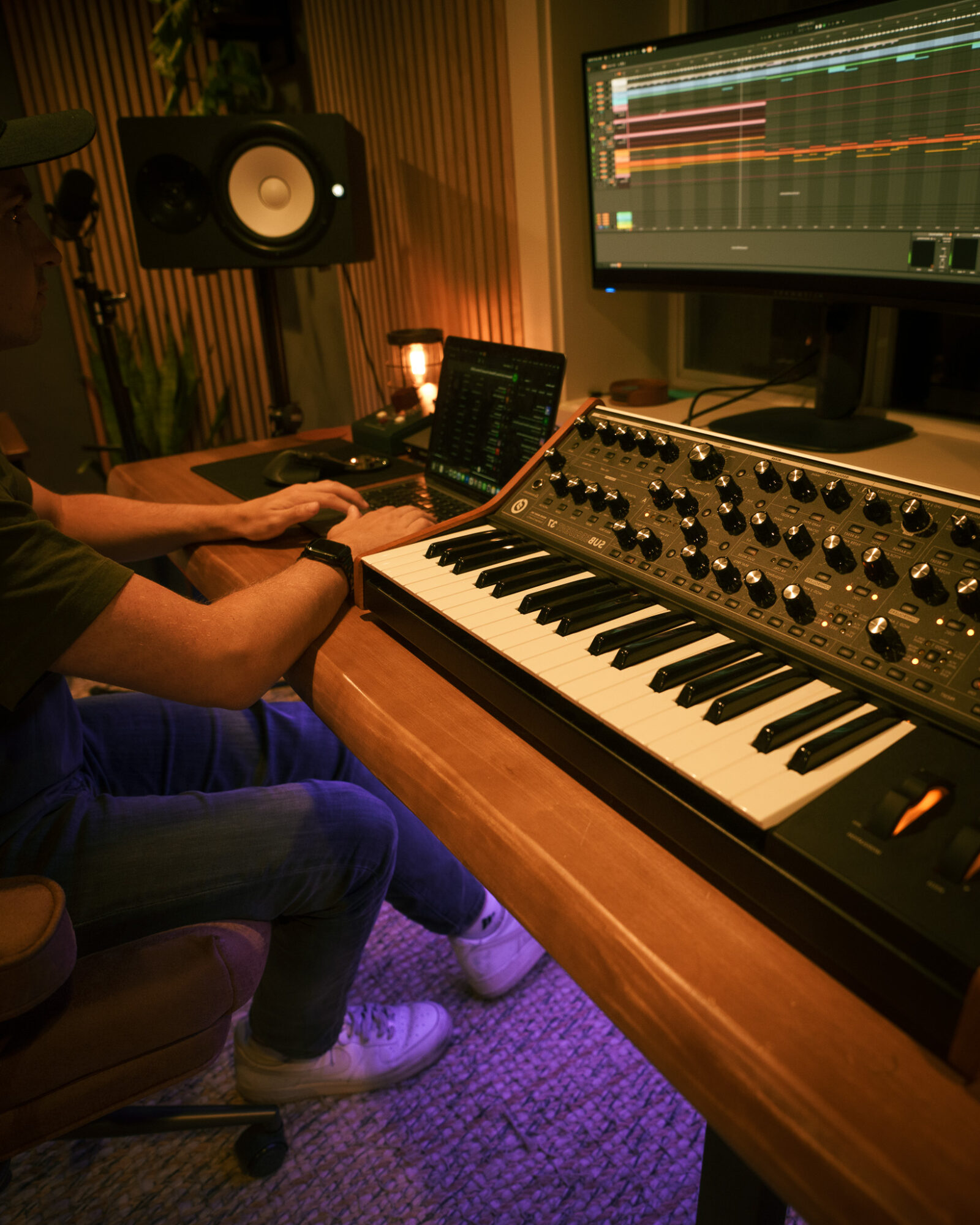 Person working on music production setup with keyboard, monitor, and audio equipment in a dimly lit room.