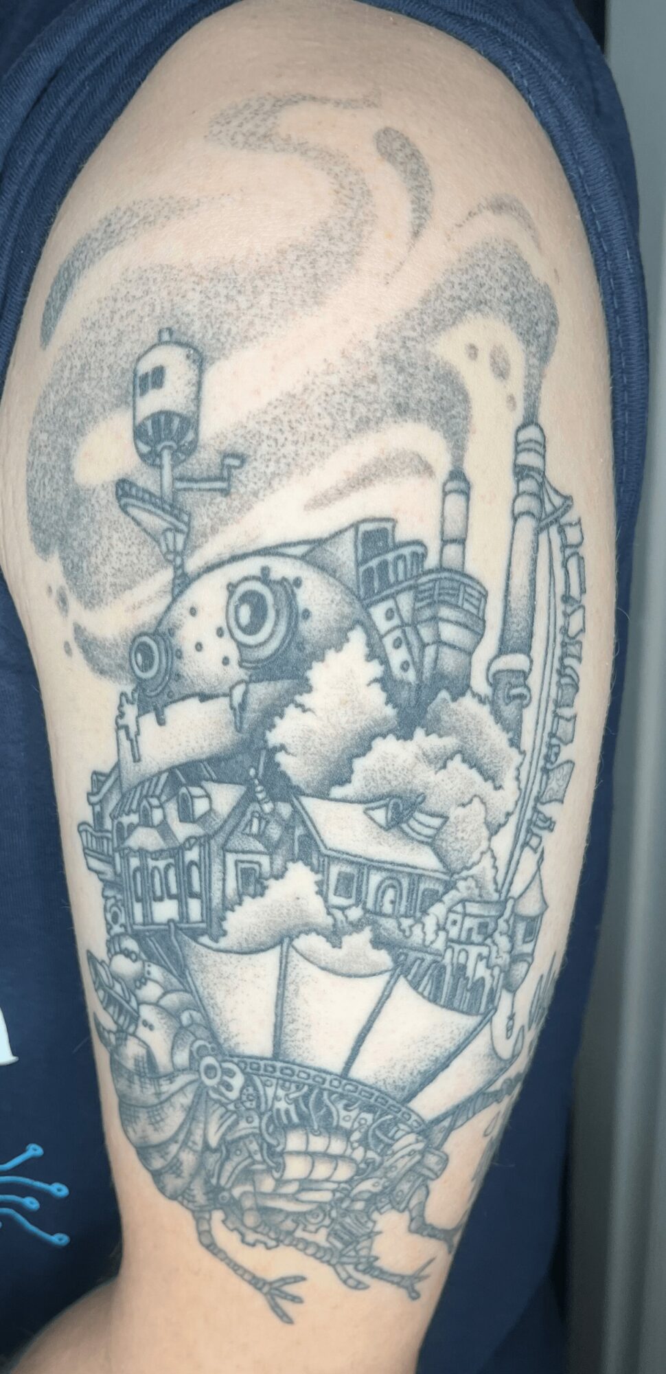 Black and gray tattoo of a steam train with smoke, on person's upper arm, detailed and realistic style.