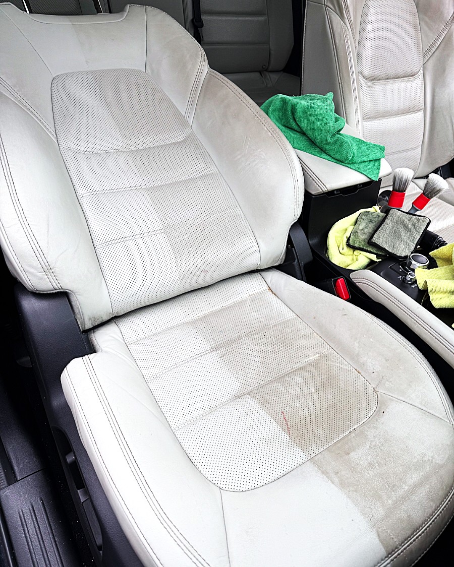Car interior with light-colored fabric seats, some items including a green cloth, yellow cloth, and electronic device on the seat.