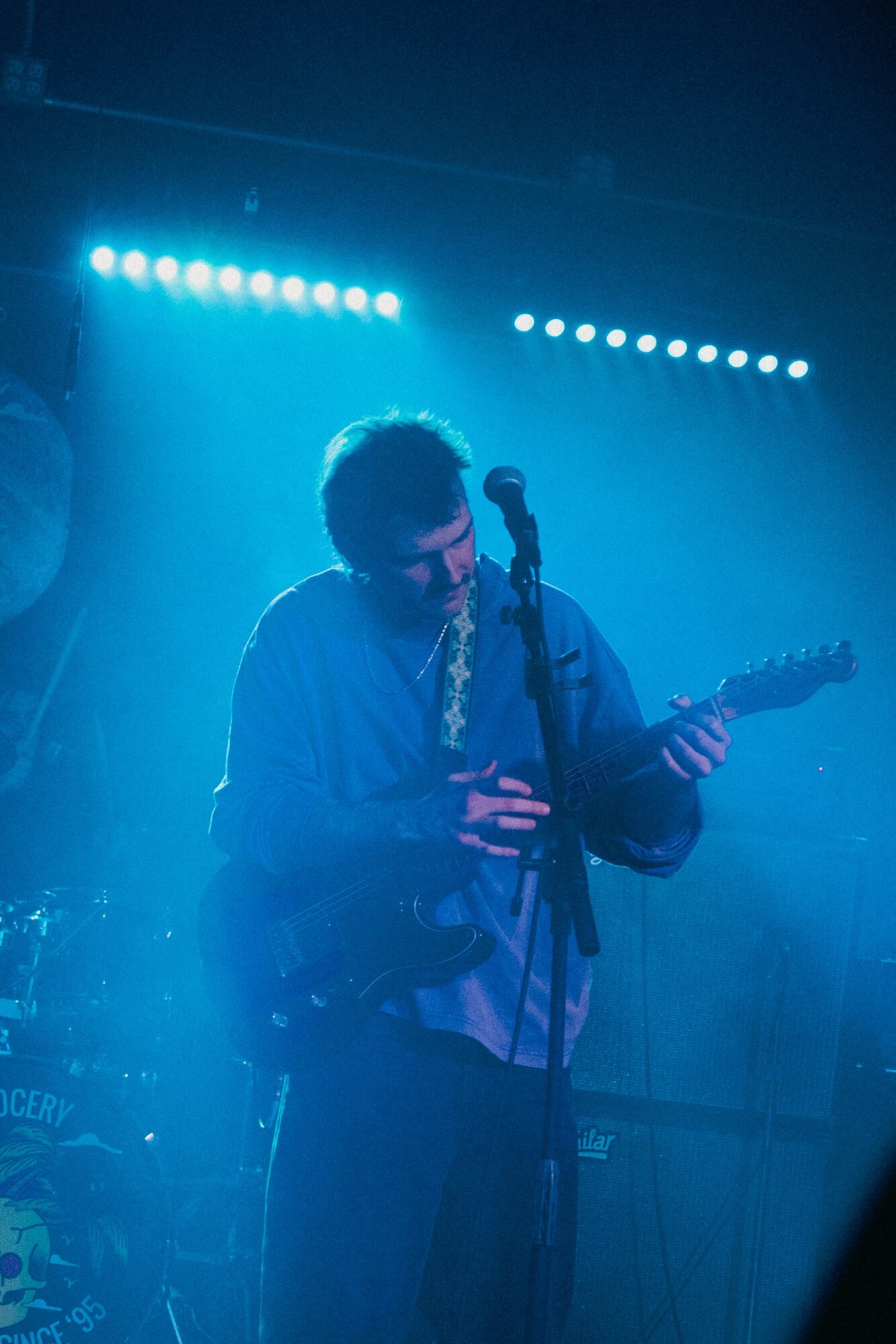 Person playing guitar on stage with blue lighting and microphone, performing live.