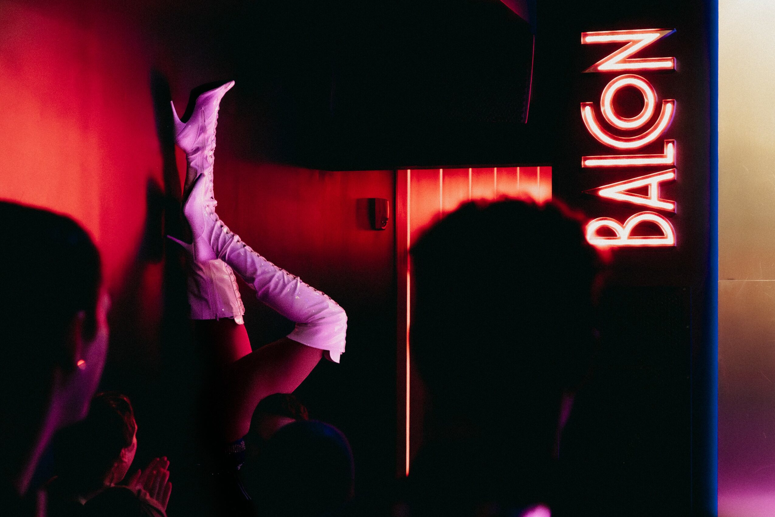 People sitting in a dimly lit room with a neon sign reading 'BALCON' on the wall.