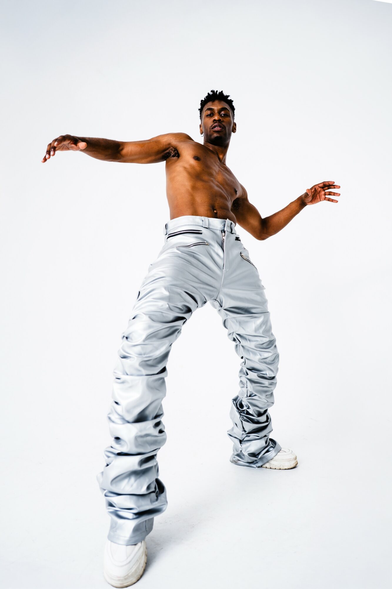A shirtless person with arms outstretched, wearing baggy pants and sneakers, standing against a plain white background.