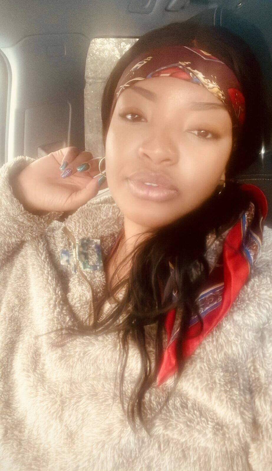 Young woman with headband and long hair, sitting in a vehicle, looking at the camera, wearing a beige sweater.