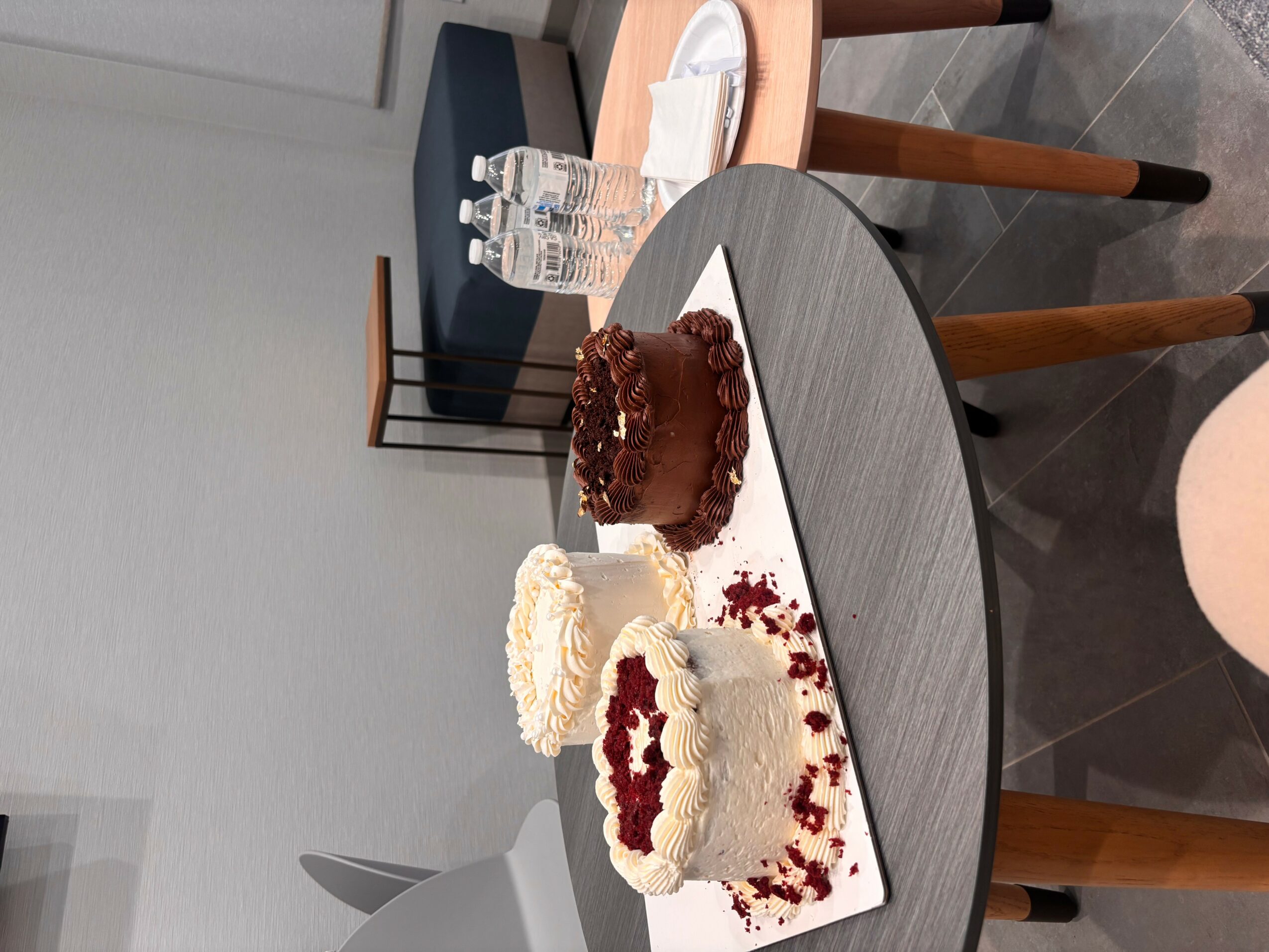 Three cakes on a table with a white and red heart-shaped cake in the center, surrounded by other cakes and drinks.