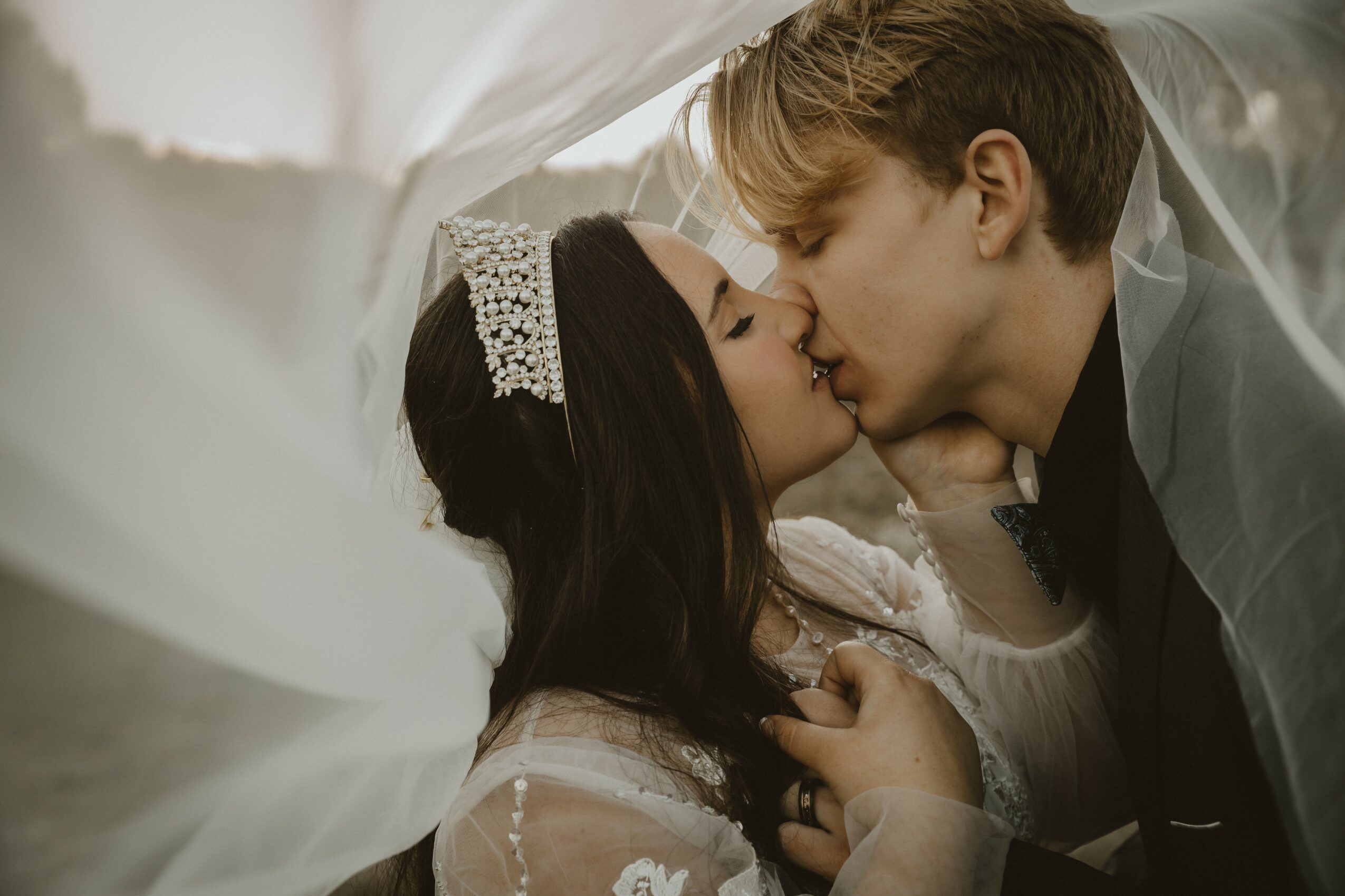 A bride and groom share a kiss, with the bride wearing a tiara and veil, and the groom in a suit.