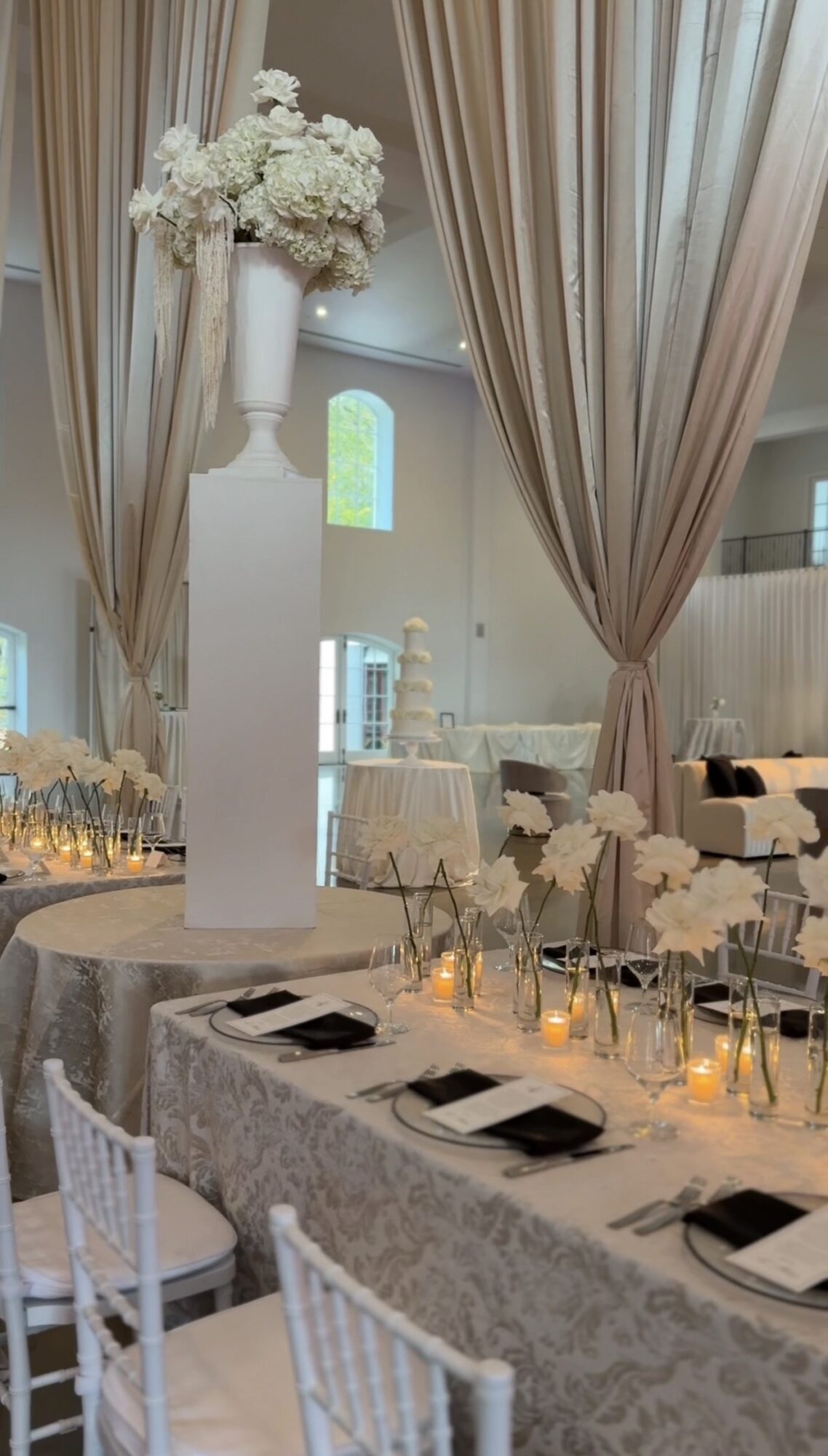 Elegant table setting with a tall floral centerpiece, candles, and neatly arranged black napkins, in a decorated event space.