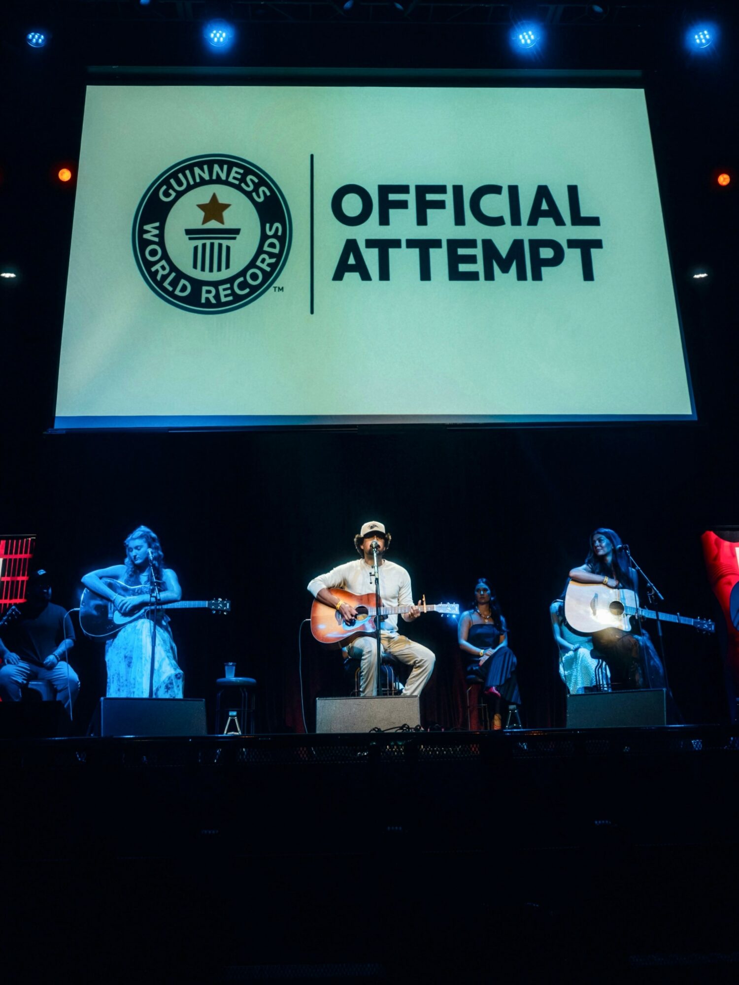 Musicians perform on stage with a large screen displaying the Guinness World Records logo and the words 'Official Attempt'.