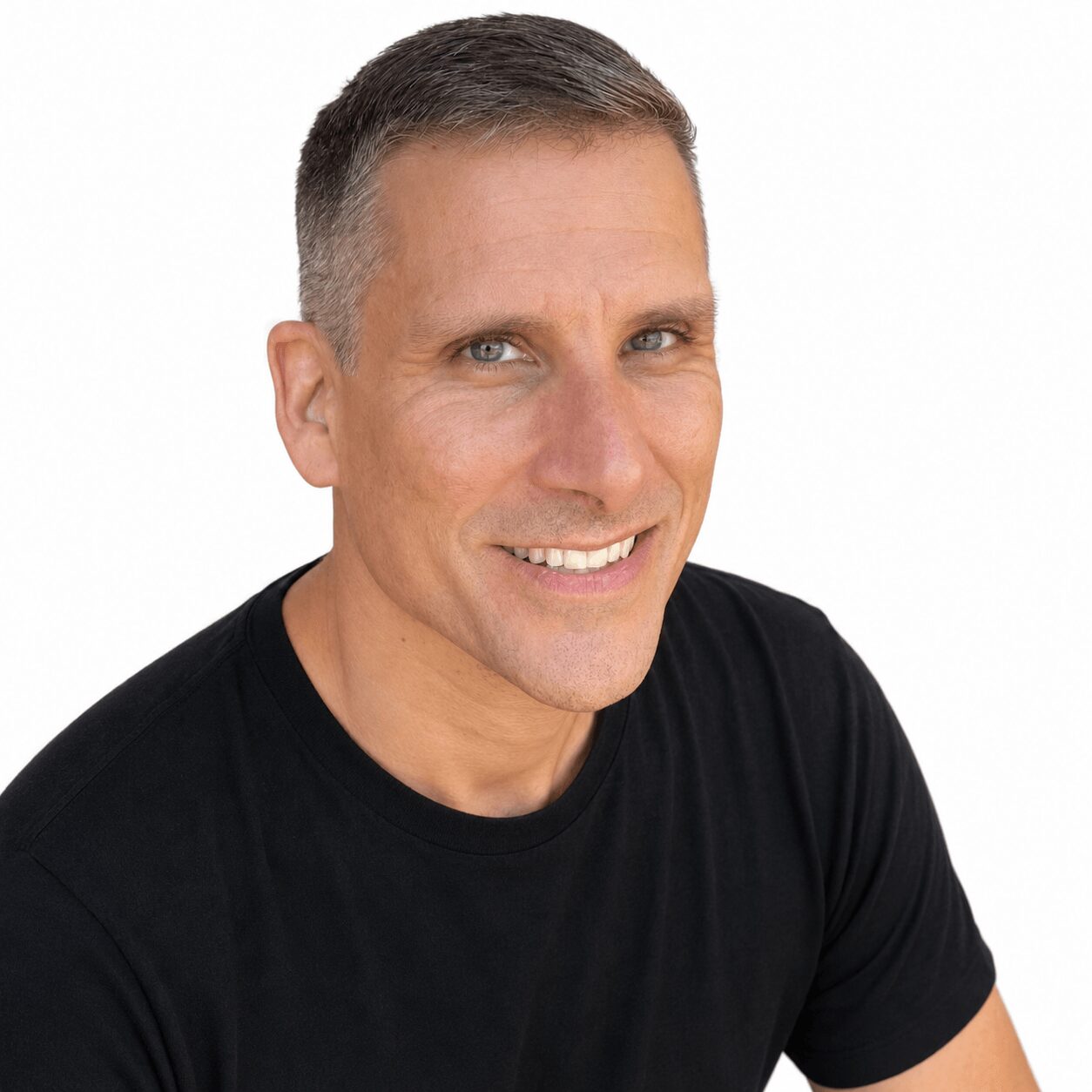 Man with short hair and a black shirt smiling against a white background.