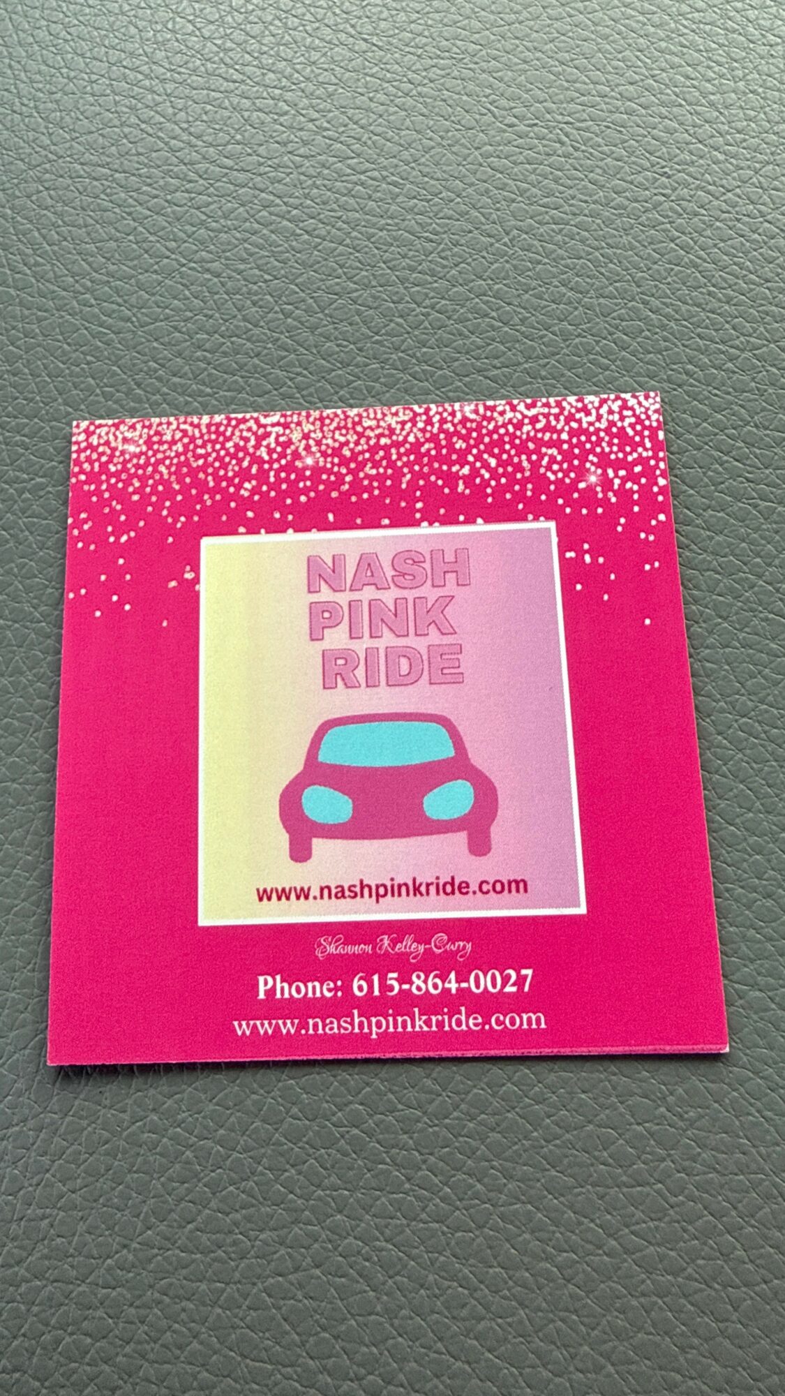 Pink flyer with a blue car illustration, text about Nash Pink Ride, and contact information, on a textured surface.