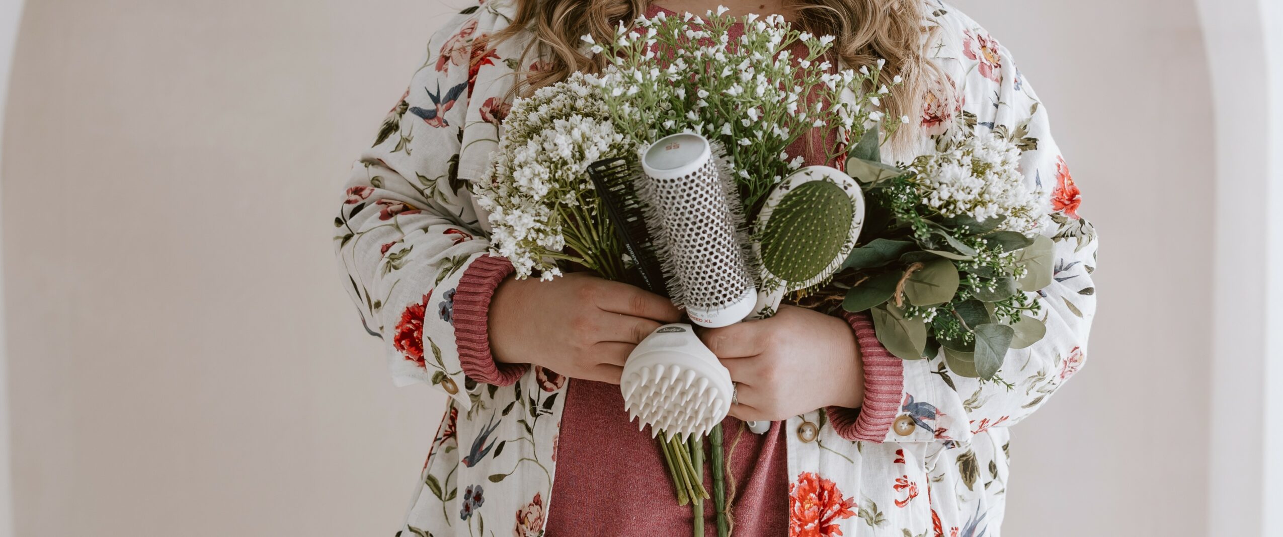 Person holding a bouquet of flowers and a rolled-up paper, wearing a floral-patterned jacket, standing indoors.