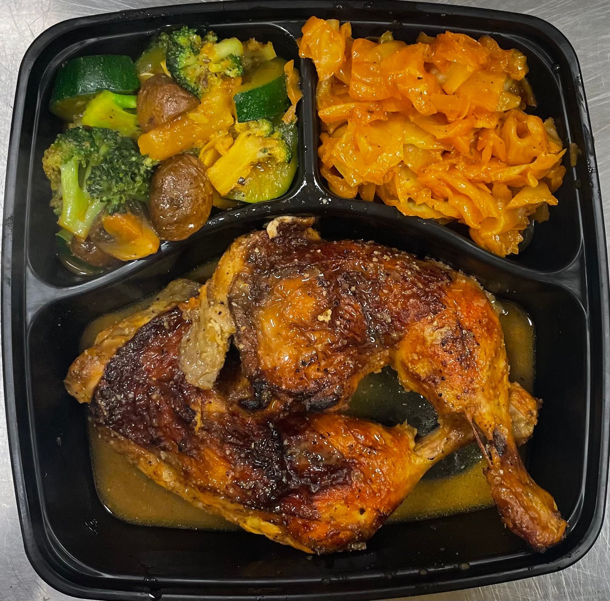 Fried chicken leg with vegetables and two side dishes in a black tray.