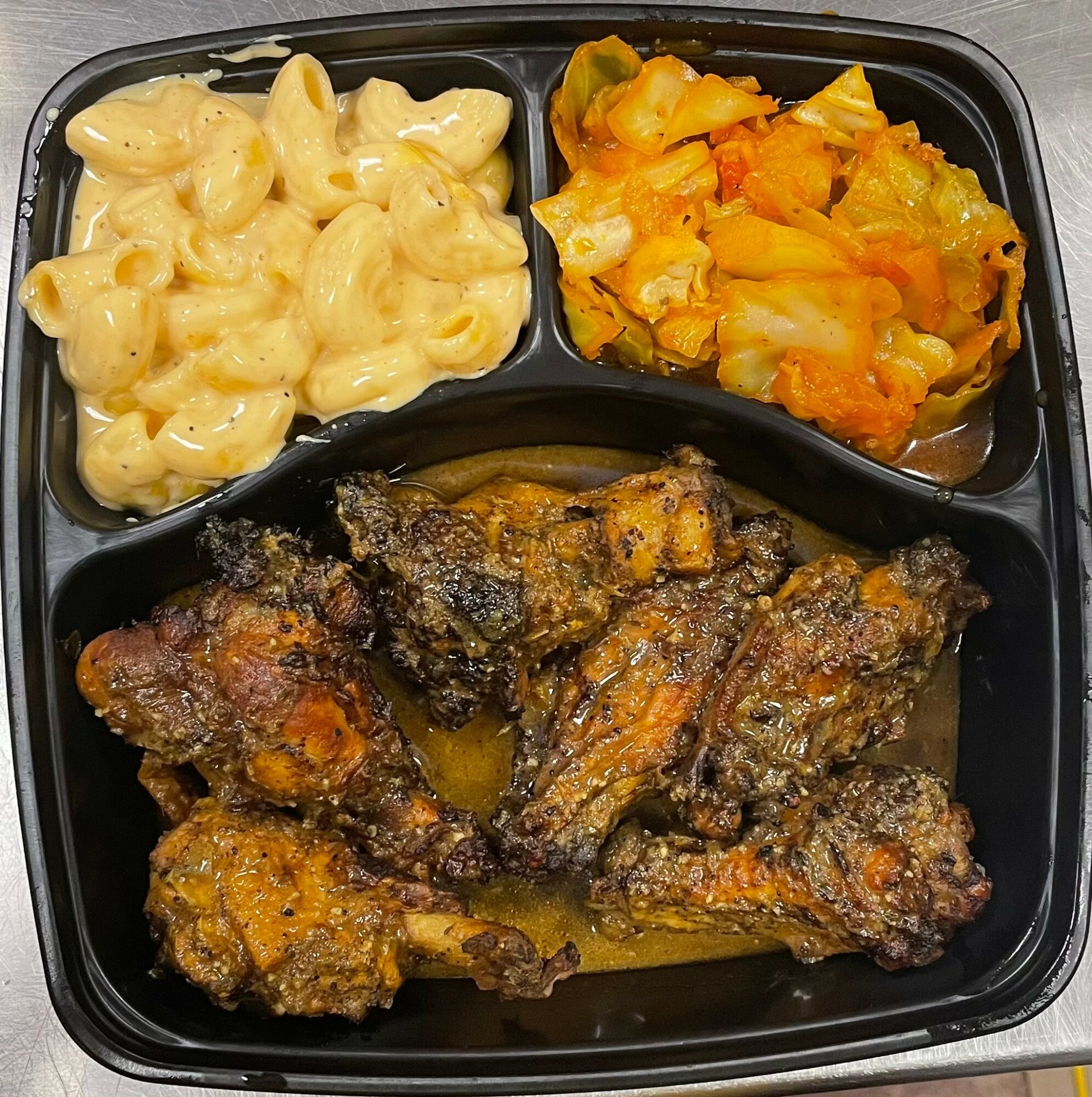 Black tray with macaroni and cheese, cooked vegetables, and fried chicken pieces.