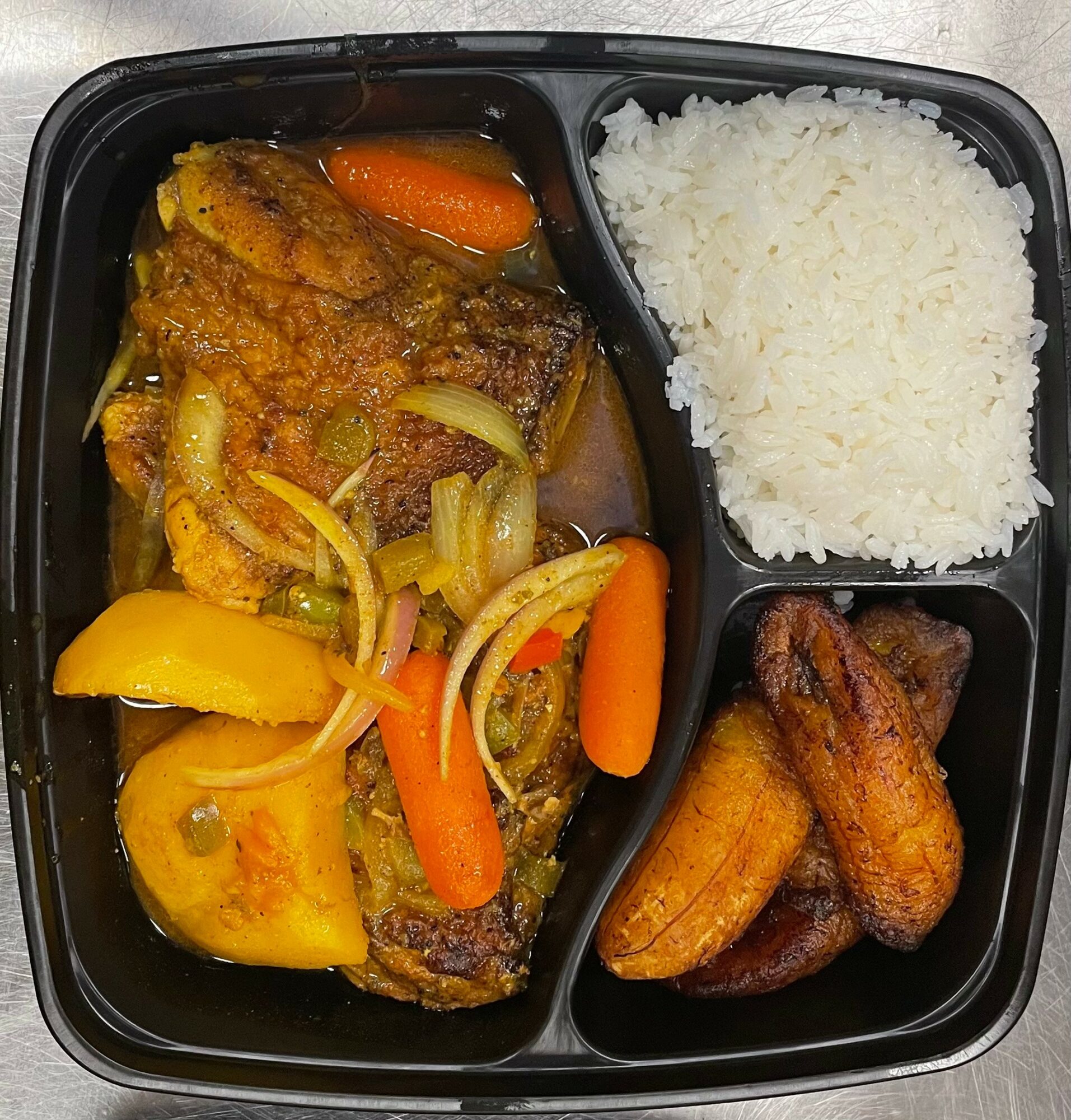 Meal with rice, fried plantains, and a vegetable and meat stew with carrots, peppers, and onions in a black container.
