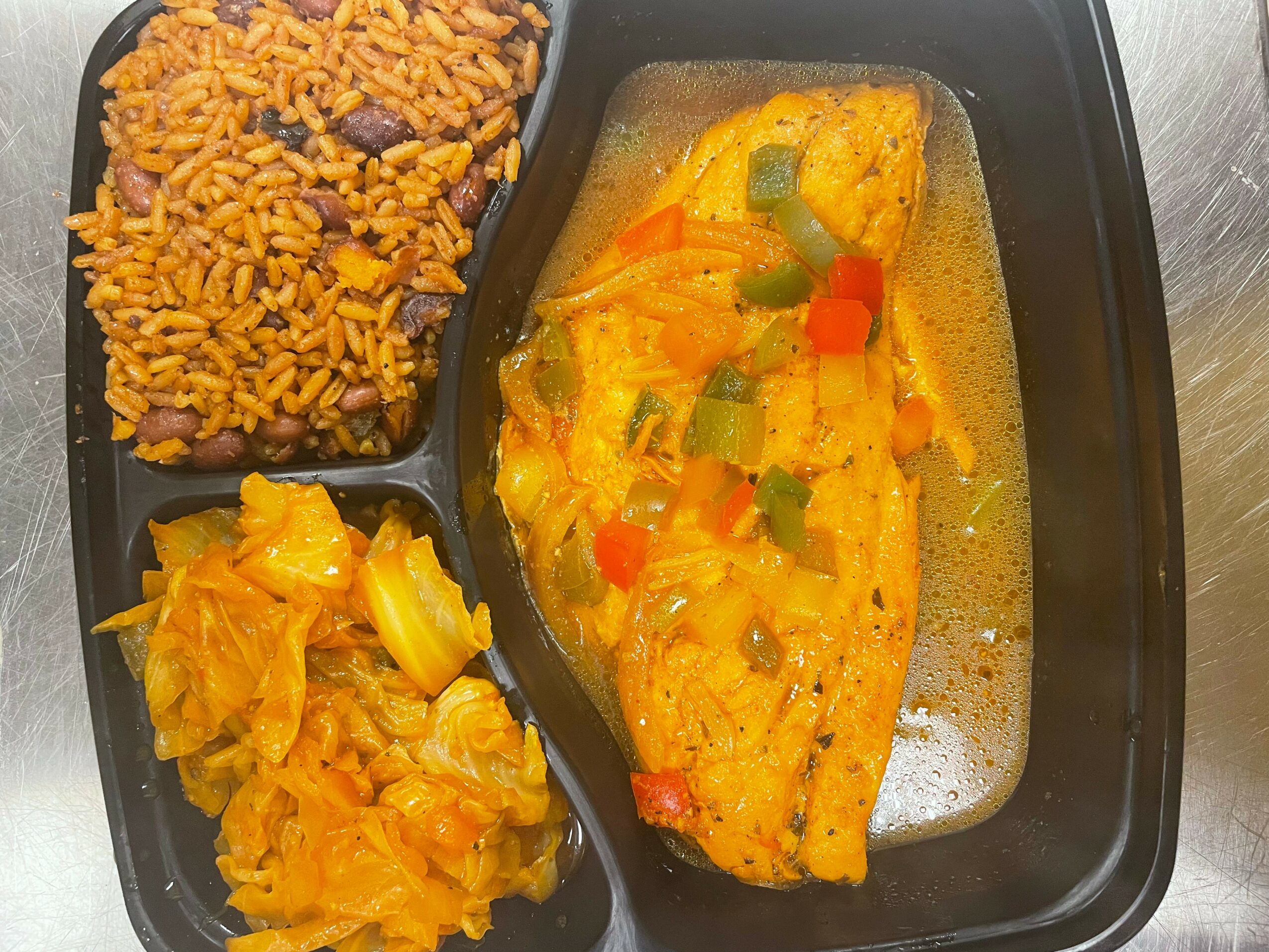 Meal tray with rice, a fish fillet with vegetables, and a side of cooked cabbage.