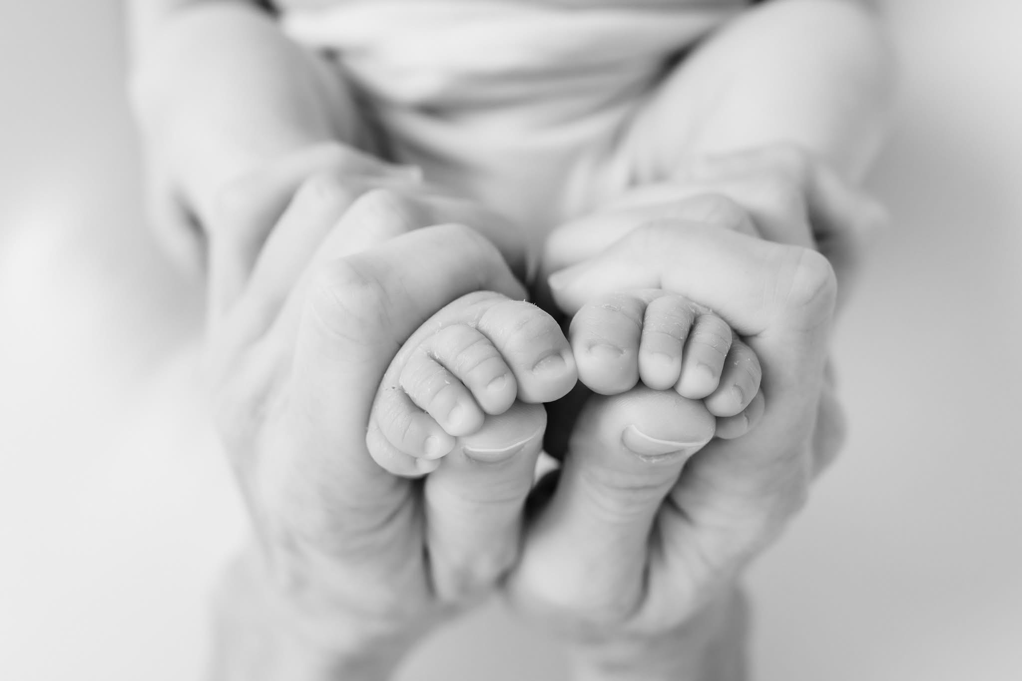 Adult holding a baby's feet with both hands, close-up in black and white.