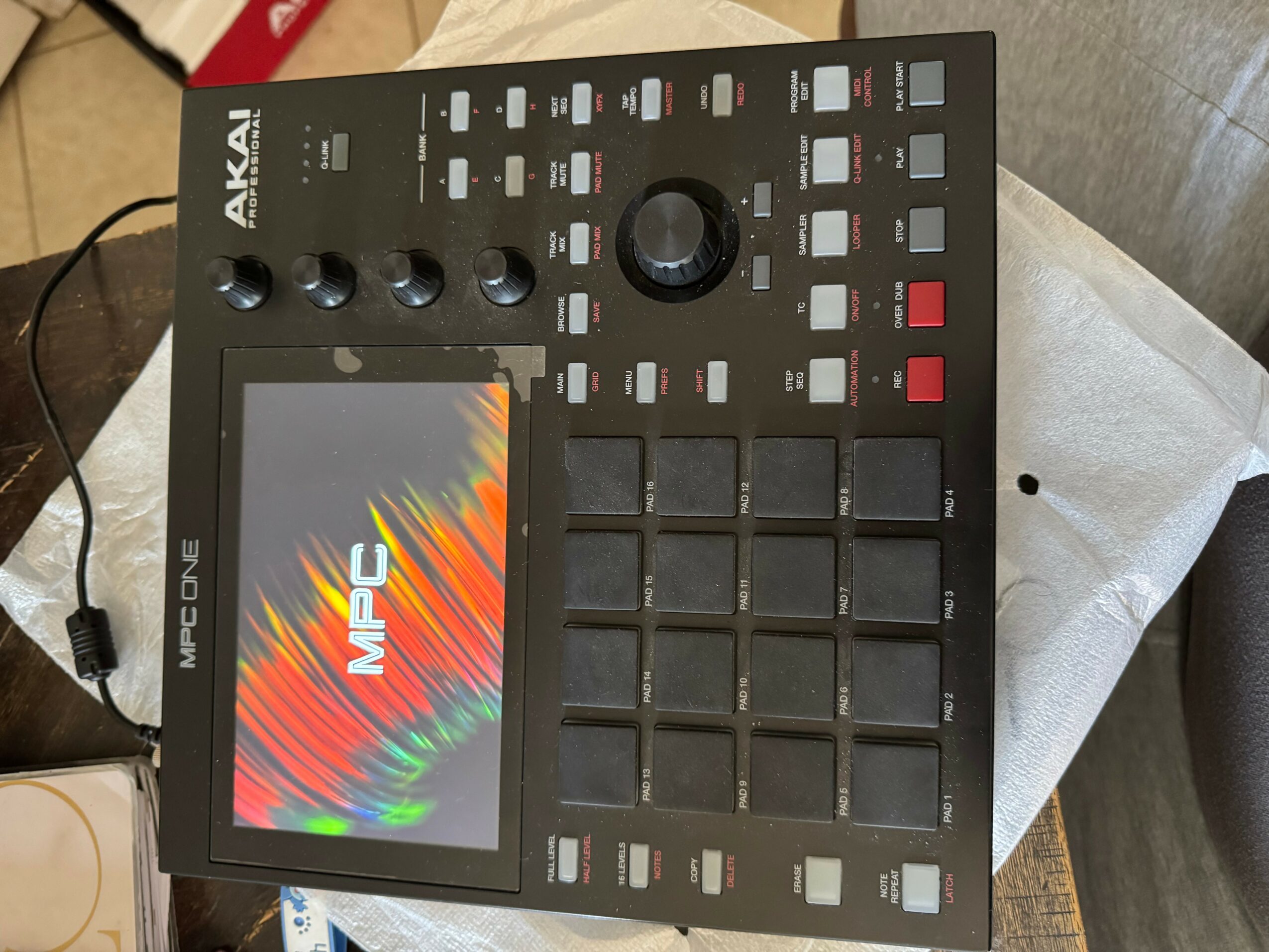 Music production device with a screen, buttons, and a large central knob on a table.