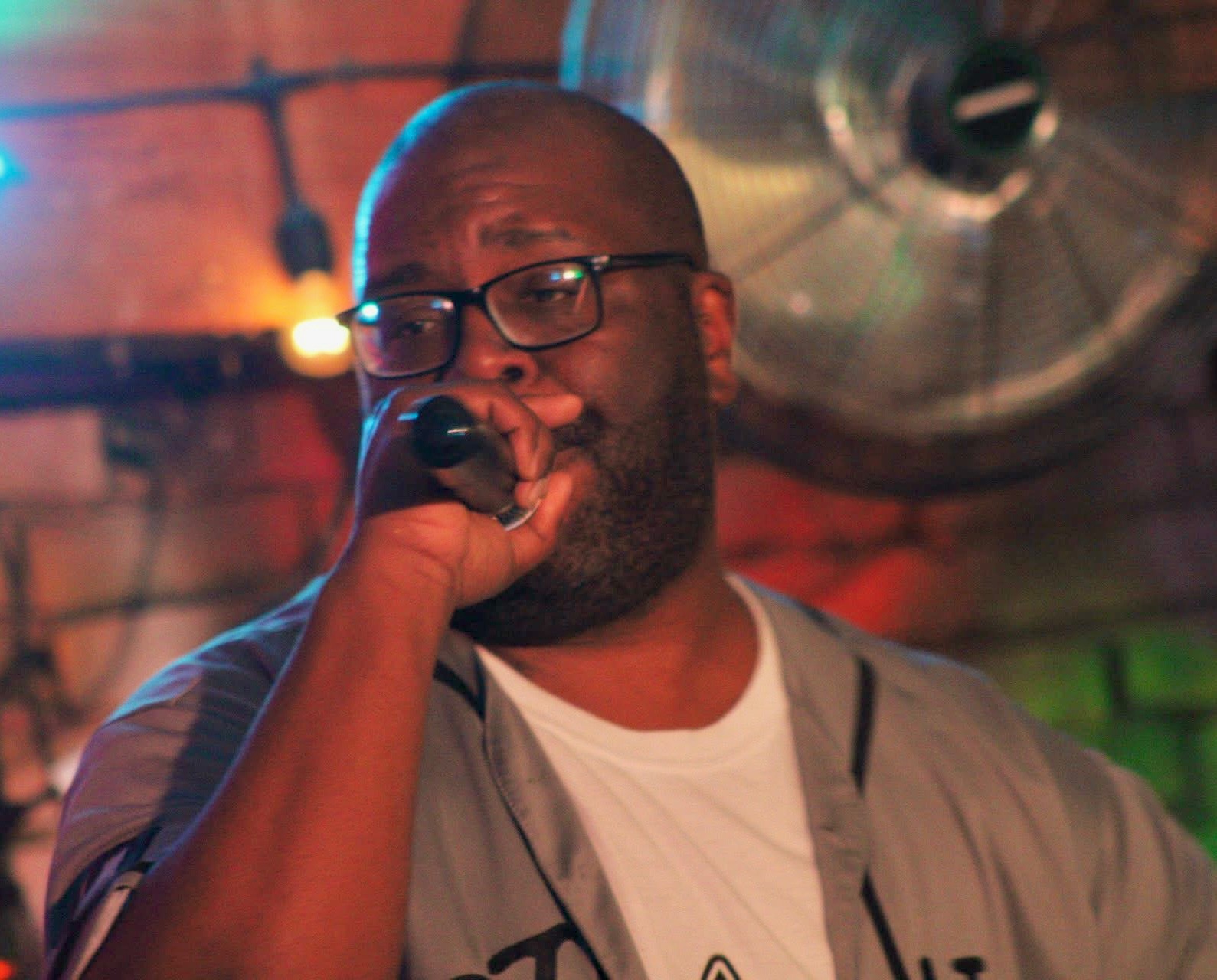 Man with glasses singing into a microphone in a dimly lit setting.
