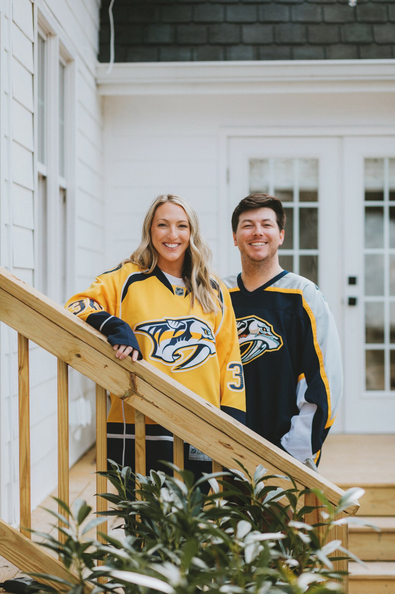 Two people in Nashville Predators hockey jerseys standing on a staircase indoors, smiling, with a white wall and window behind them.