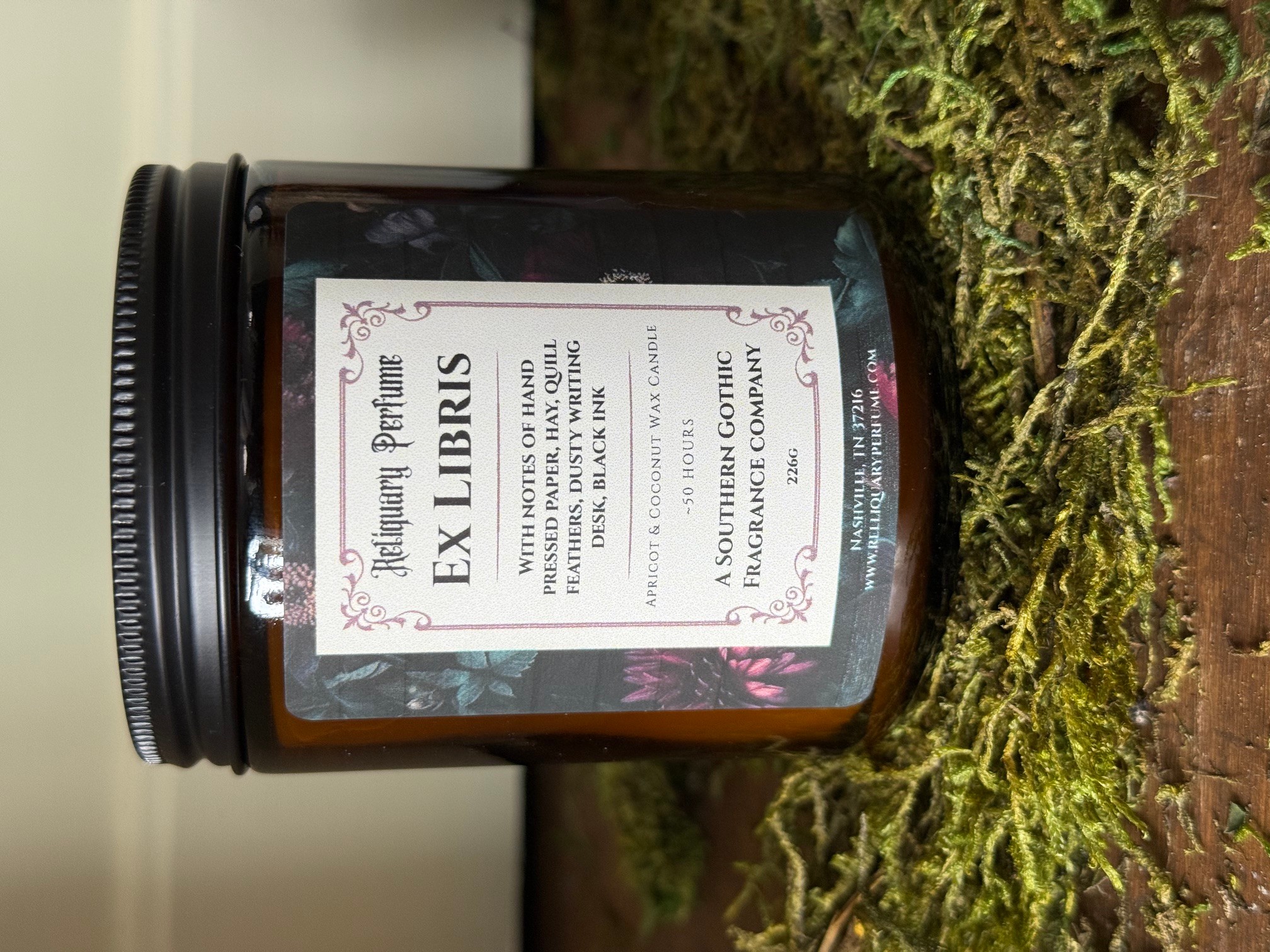 A jar labeled 'Ex Libris' on mossy wood surface, with a white background and decorative border, viewed sideways.