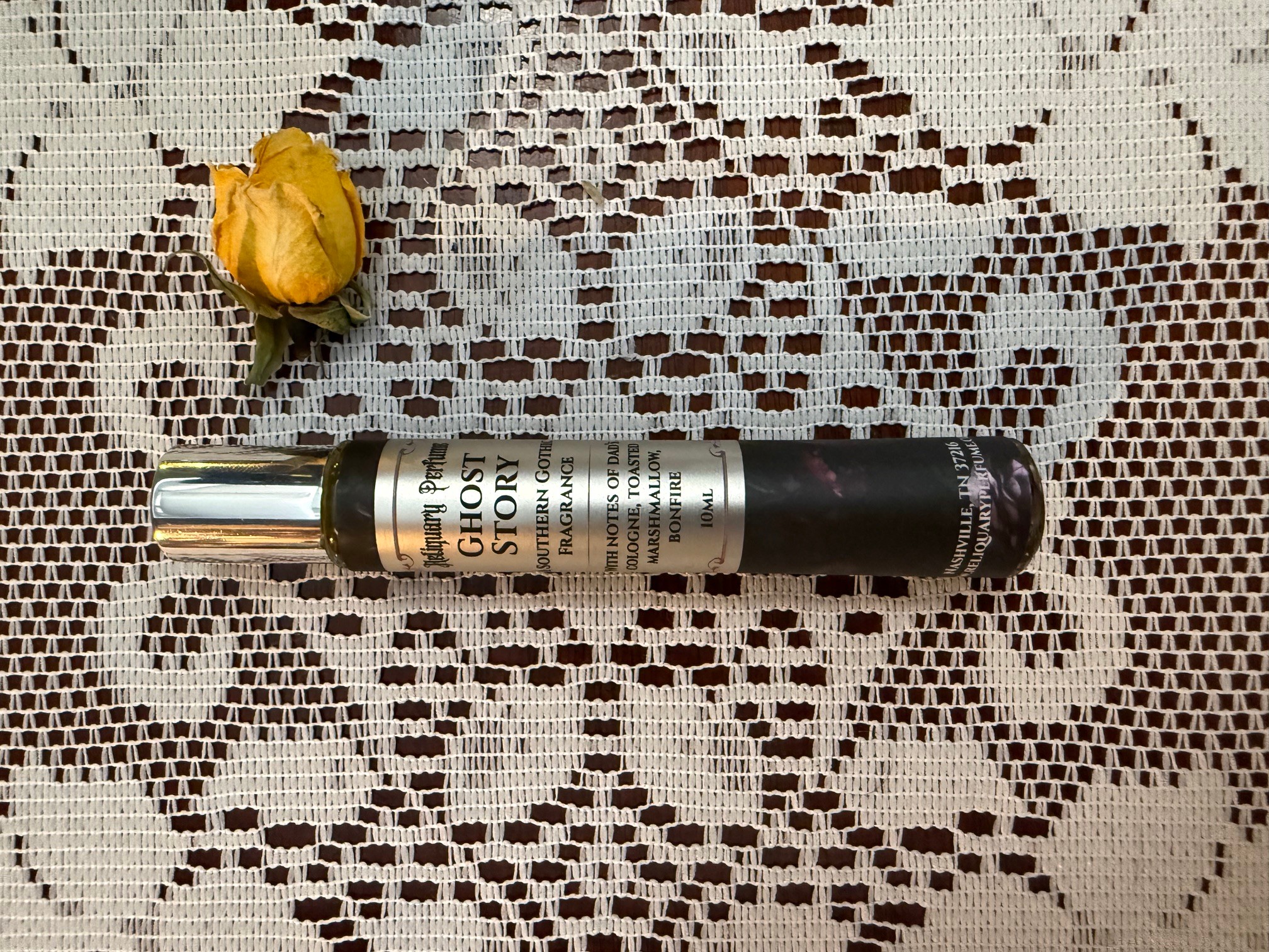 A small yellow flower and a black and silver spray bottle on a lace tablecloth, viewed from above.