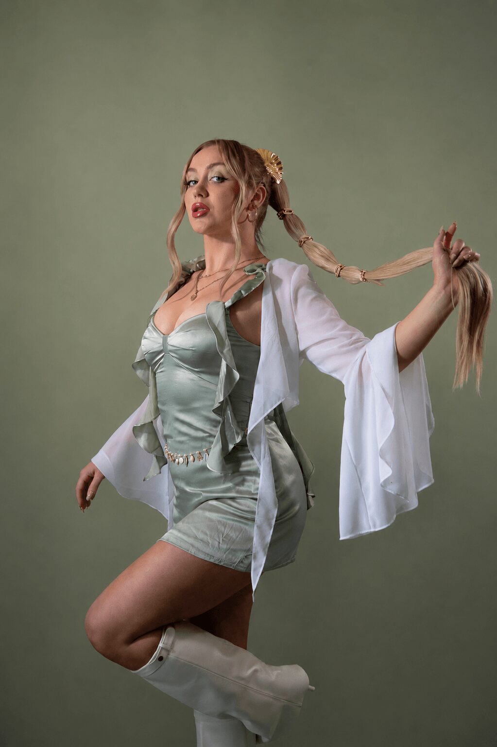 Young woman with long braided hair, wearing a shiny silver outfit and white jacket, poses against a plain background.