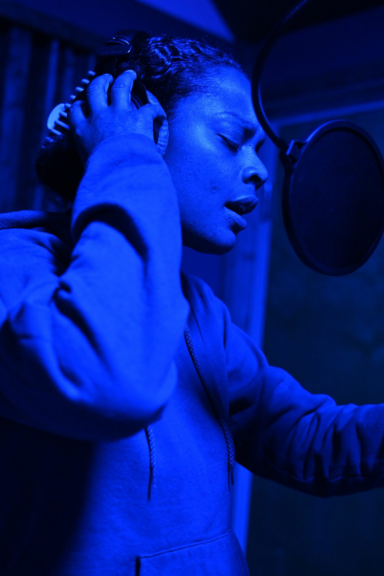 Person with headphones leaning forward, face close to a microphone, in blue lighting.