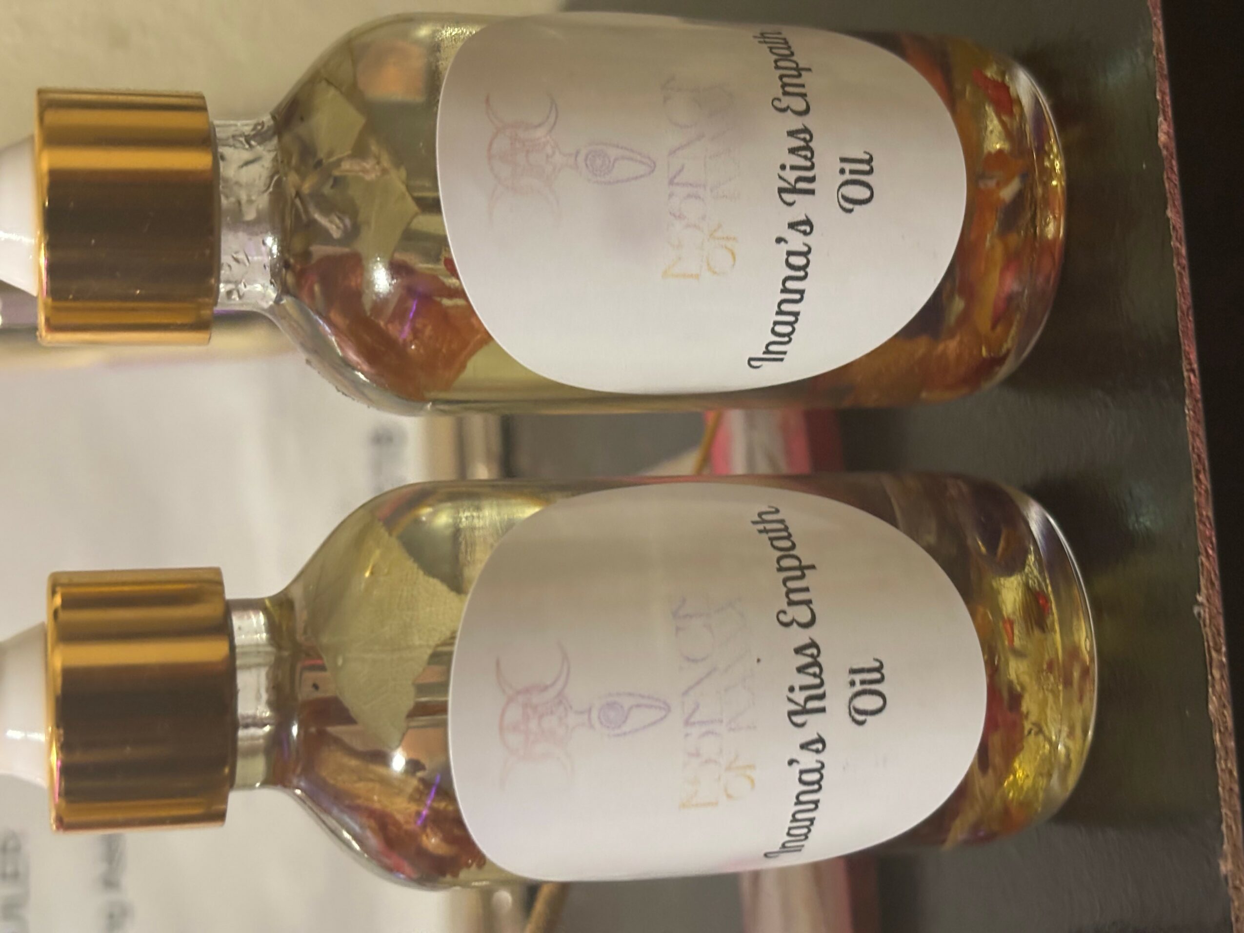 Two glass bottles with gold caps and white labels, lying horizontally on a surface, with liquid inside.