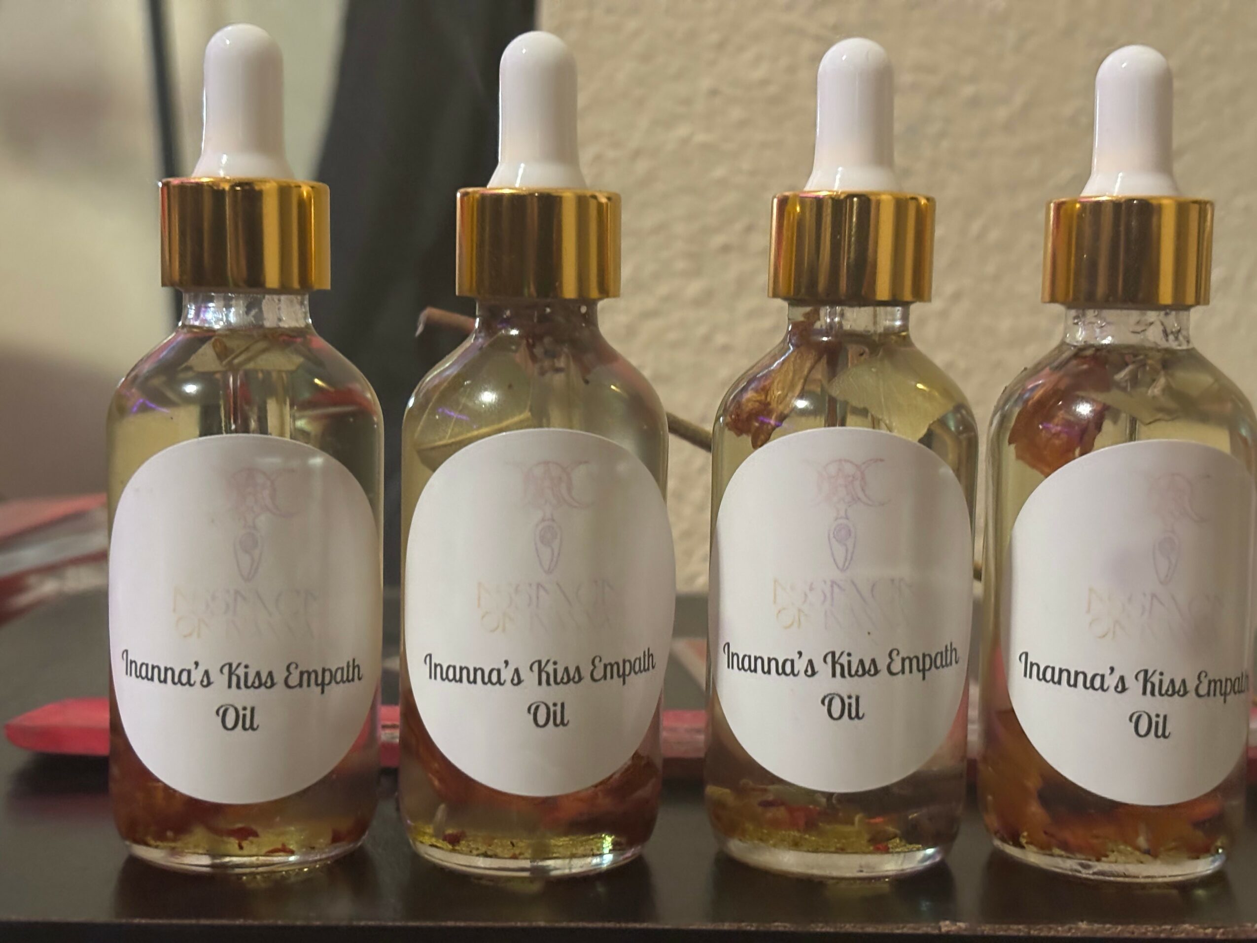 Four small glass bottles with white labels and dropper caps, labeled 'Inanna's Kiss Empan Oil', lined up on a surface.