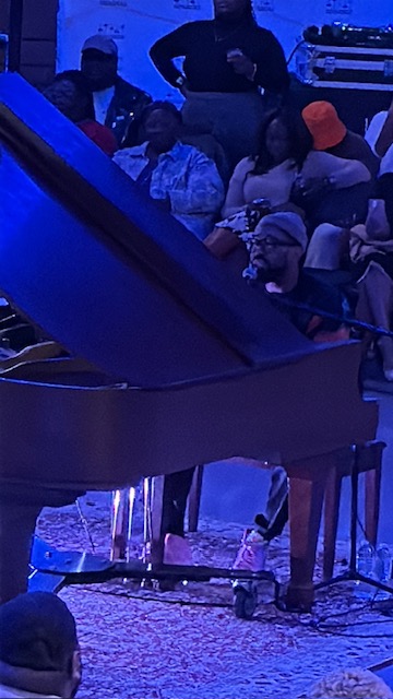 People sitting around a grand piano in a dimly lit room with blue lighting.