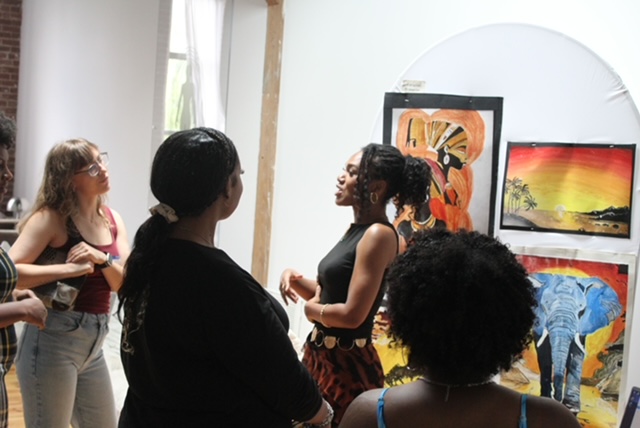 Group of people in an art gallery looking at colorful paintings on the wall.