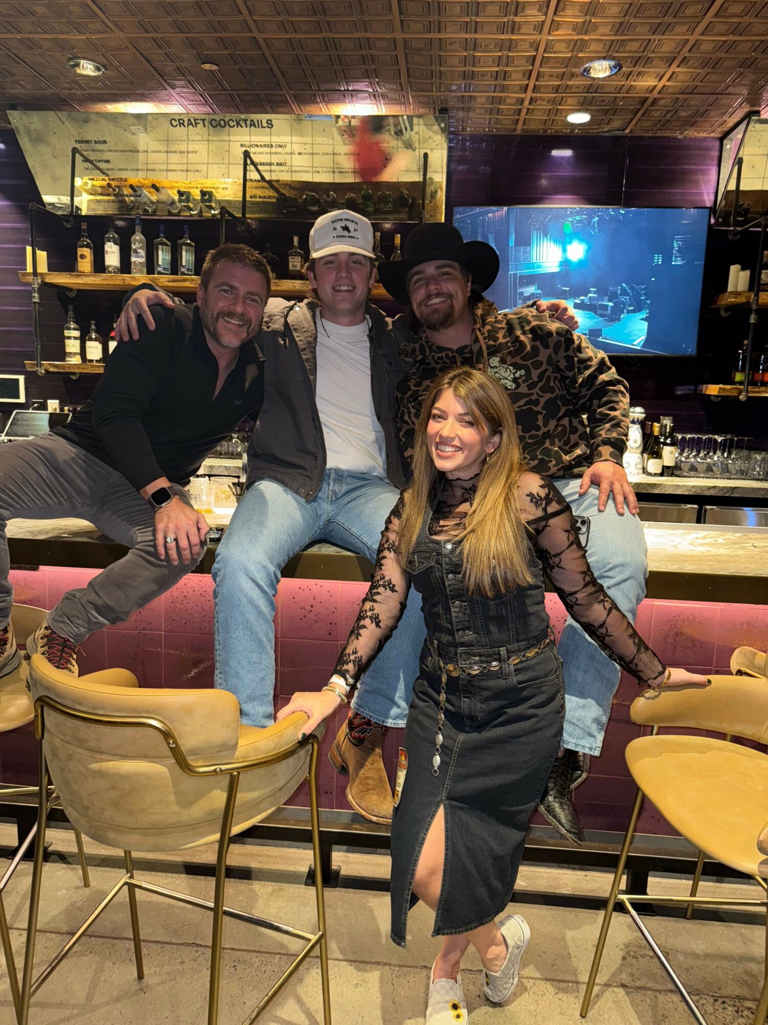 Group of five people sitting and standing around a table in a restaurant or bar, smiling and posing for the photo.