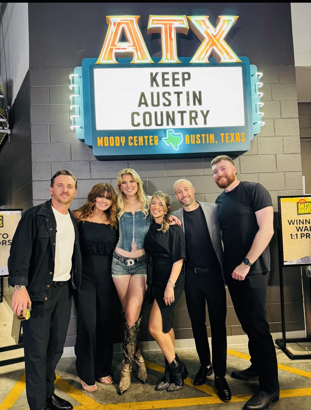 Group of five people standing in front of a sign that reads 'ATX Keep Austin Country' at Moody Center, Austin, Texas.