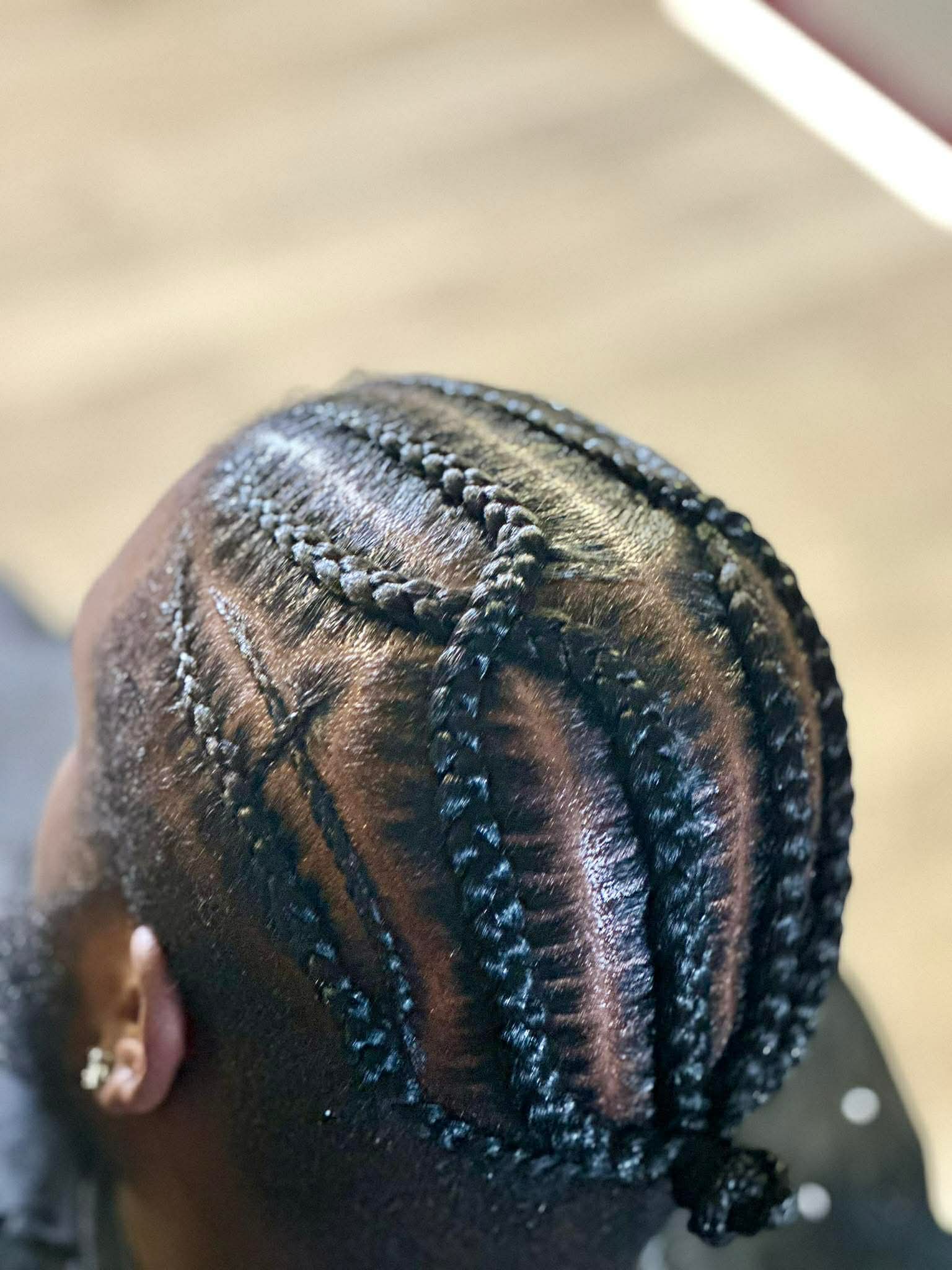 Top view of a person's head with braided hairstyle, showing intricate cornrows and beads, on a wooden surface.