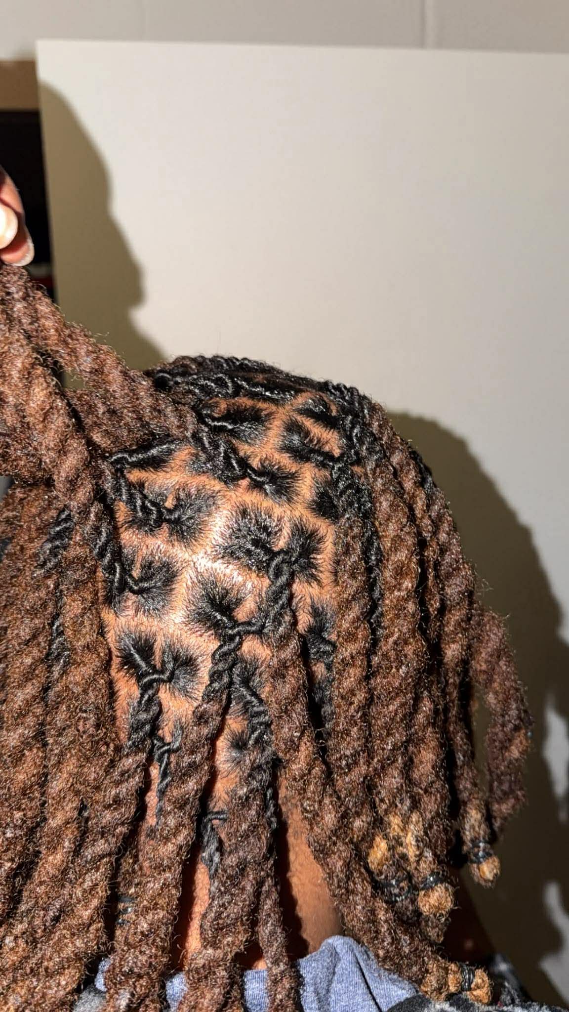Close-up of a person's head with styled, textured, brown hair and a patterned garment visible.