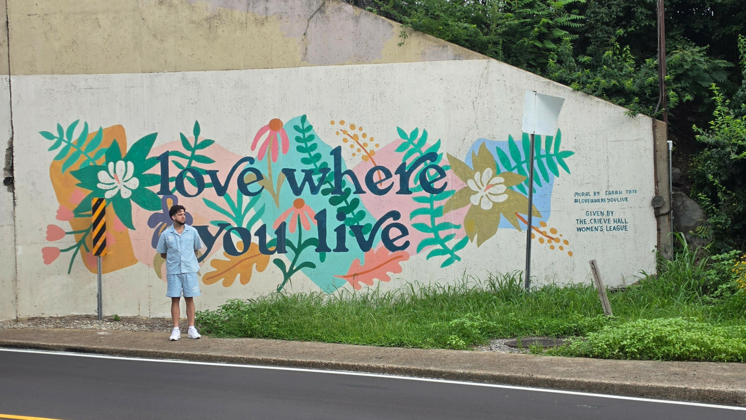 Person standing in front of a colorful mural with flowers and text on a wall.