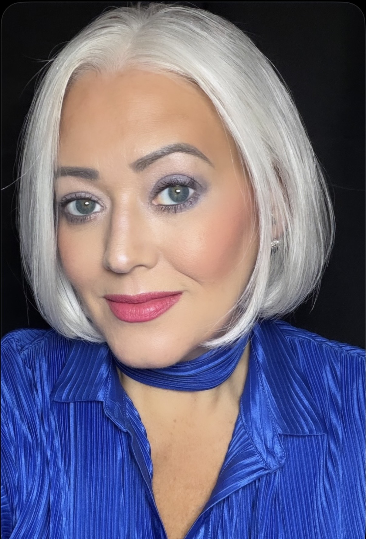 Portrait of a woman with short white hair, blue eyes, wearing a blue top, smiling.