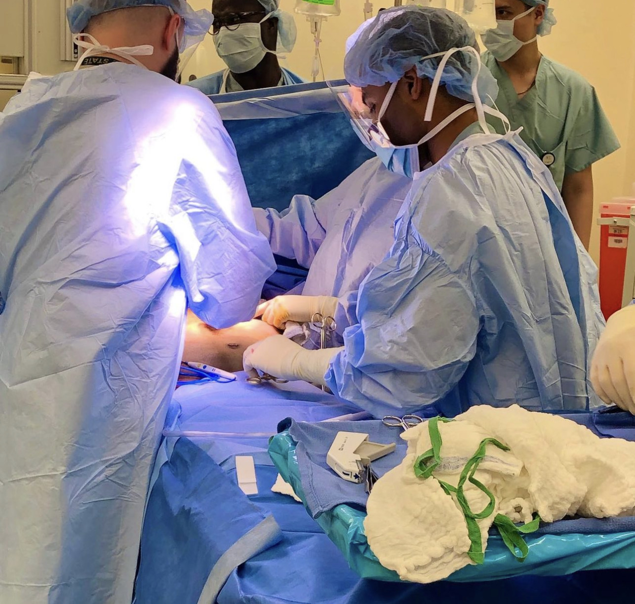 Medical team performs surgery in operating room with surgical tools and equipment, wearing protective gowns and masks.